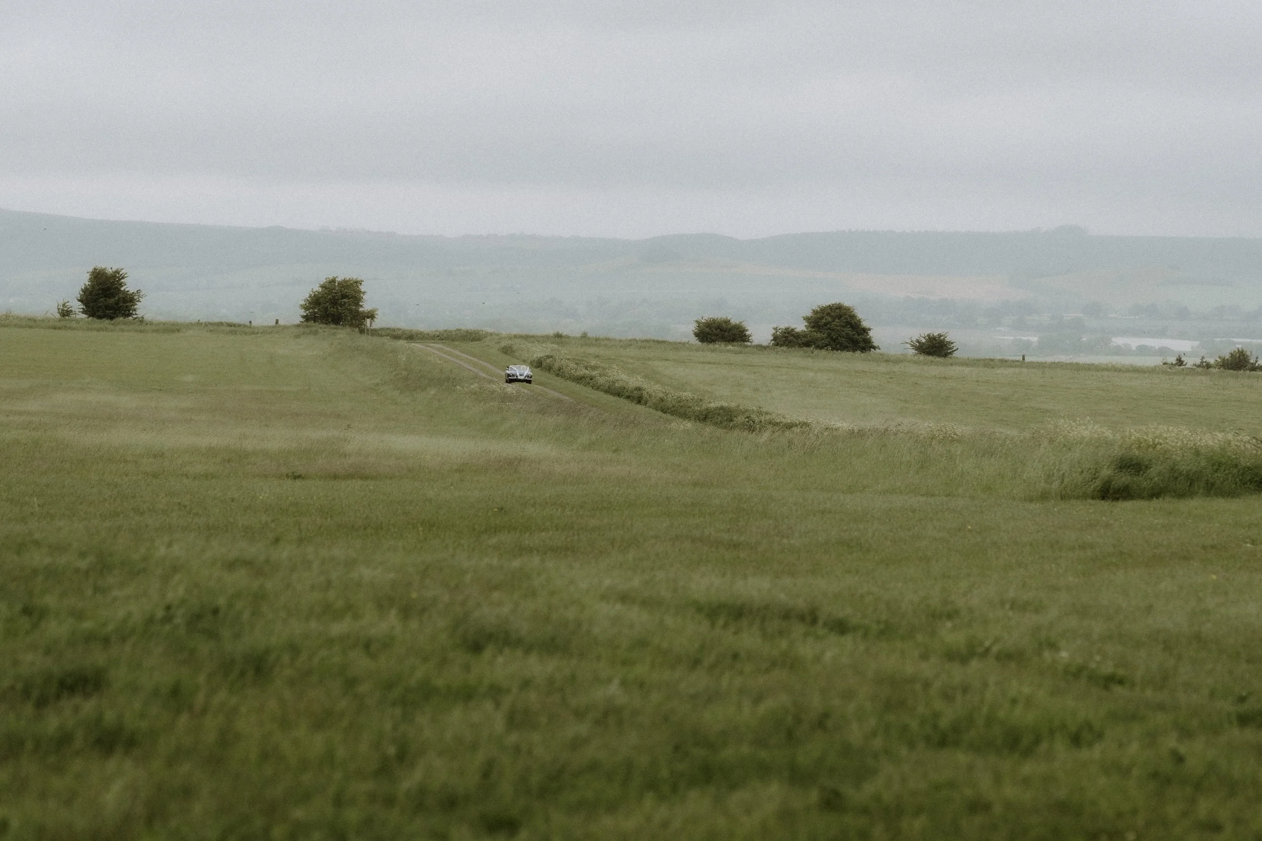 A vintage car driving through the Wiltshire countryside to a spring wedding reception