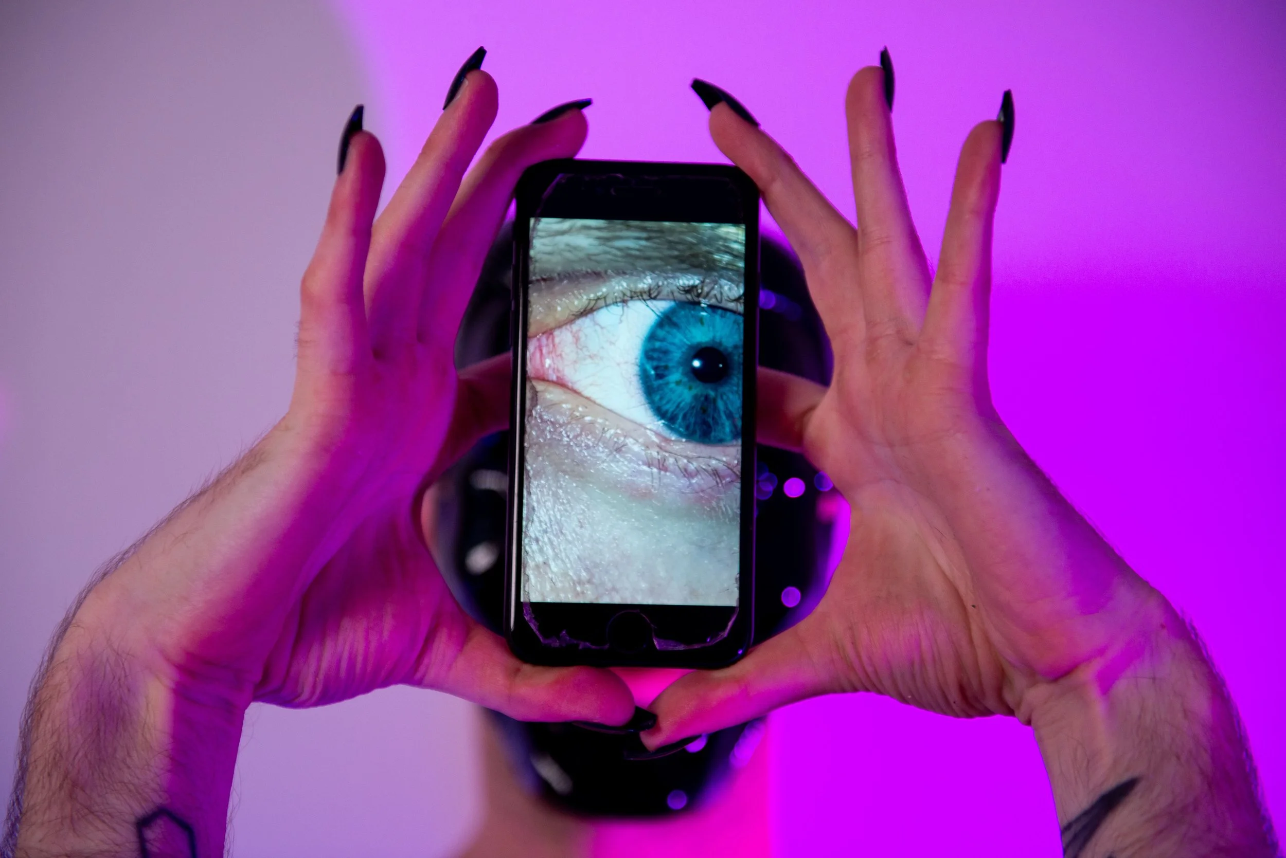 Ave Vanilla - Enfant Terrible: A conceptual close-up of hands holding a smartphone displaying a detailed human eye, exploring themes of voyeurism and digital presence[cite: 40].