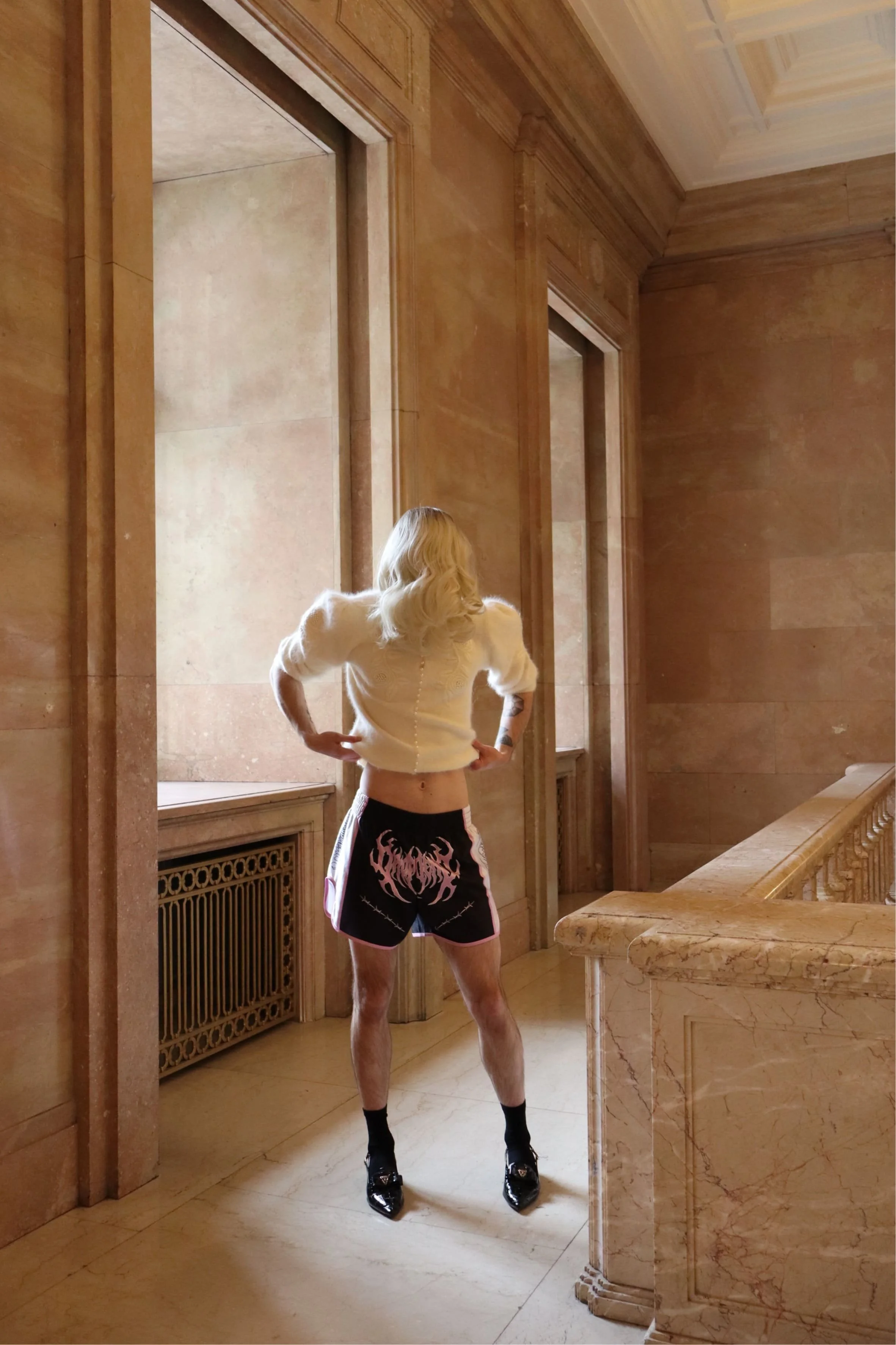 Performer standing in a wooden interior facing the wall - Ave Vanilla performance art, site-responsive work