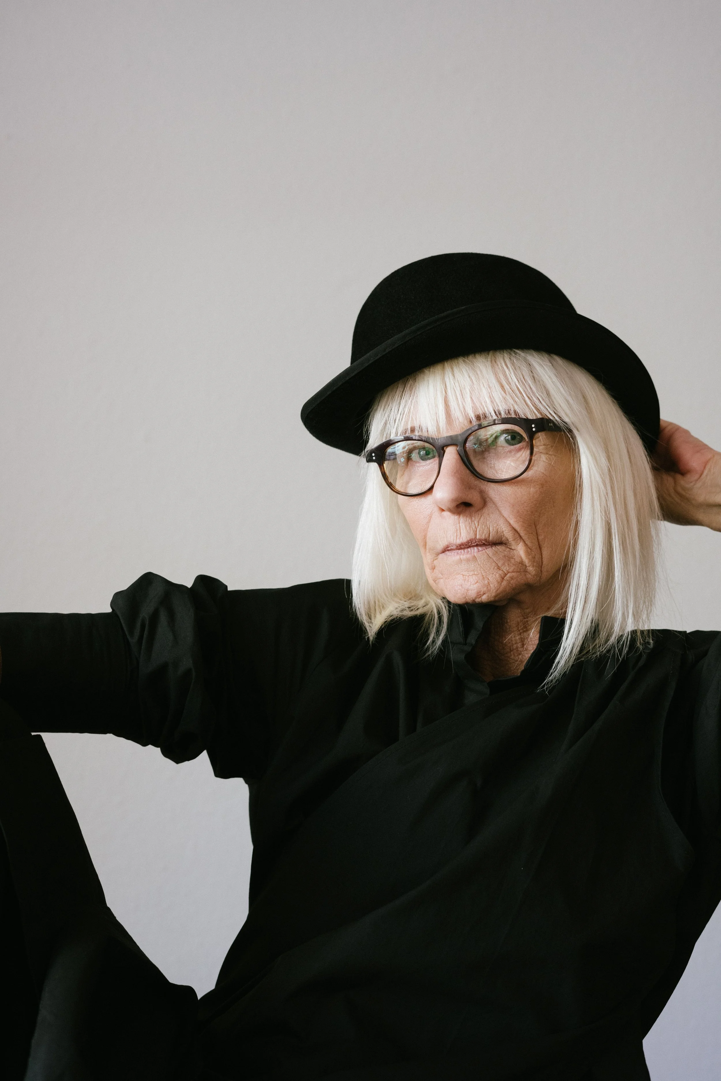 Elderly woman with white hair, wearing glasses, a black hat, and a black outfit.
