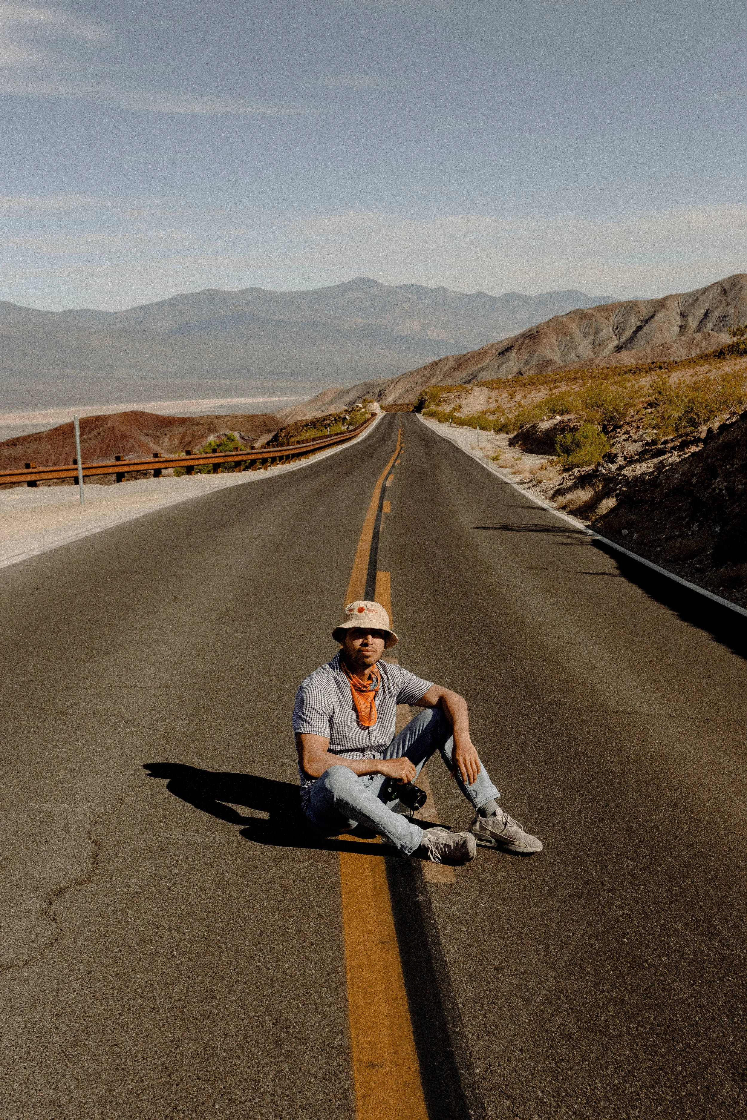Person sitting on a deserted road in a desert landscape with mountains in the background.