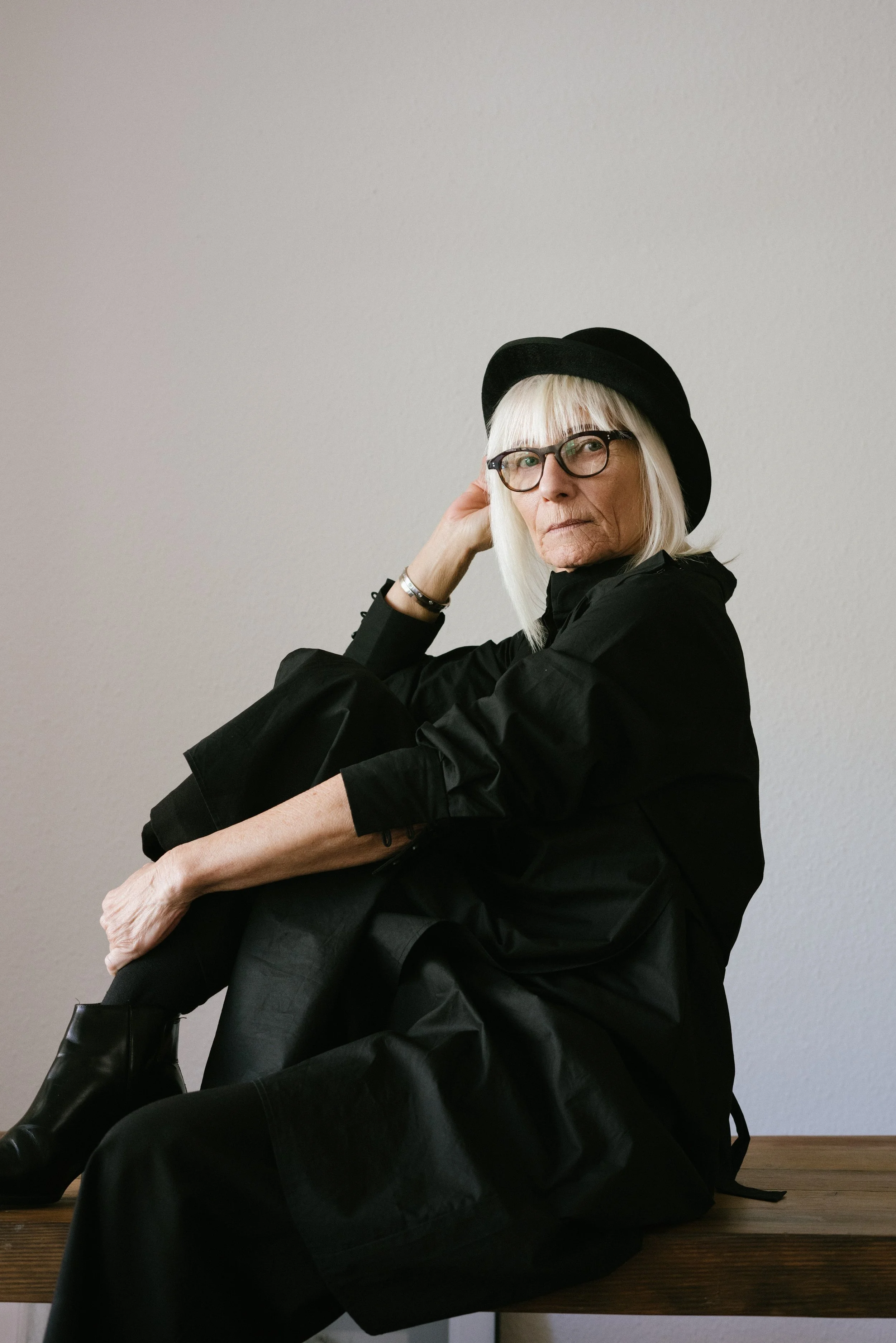 Elderly woman wearing black attire and hat sitting on a bench
