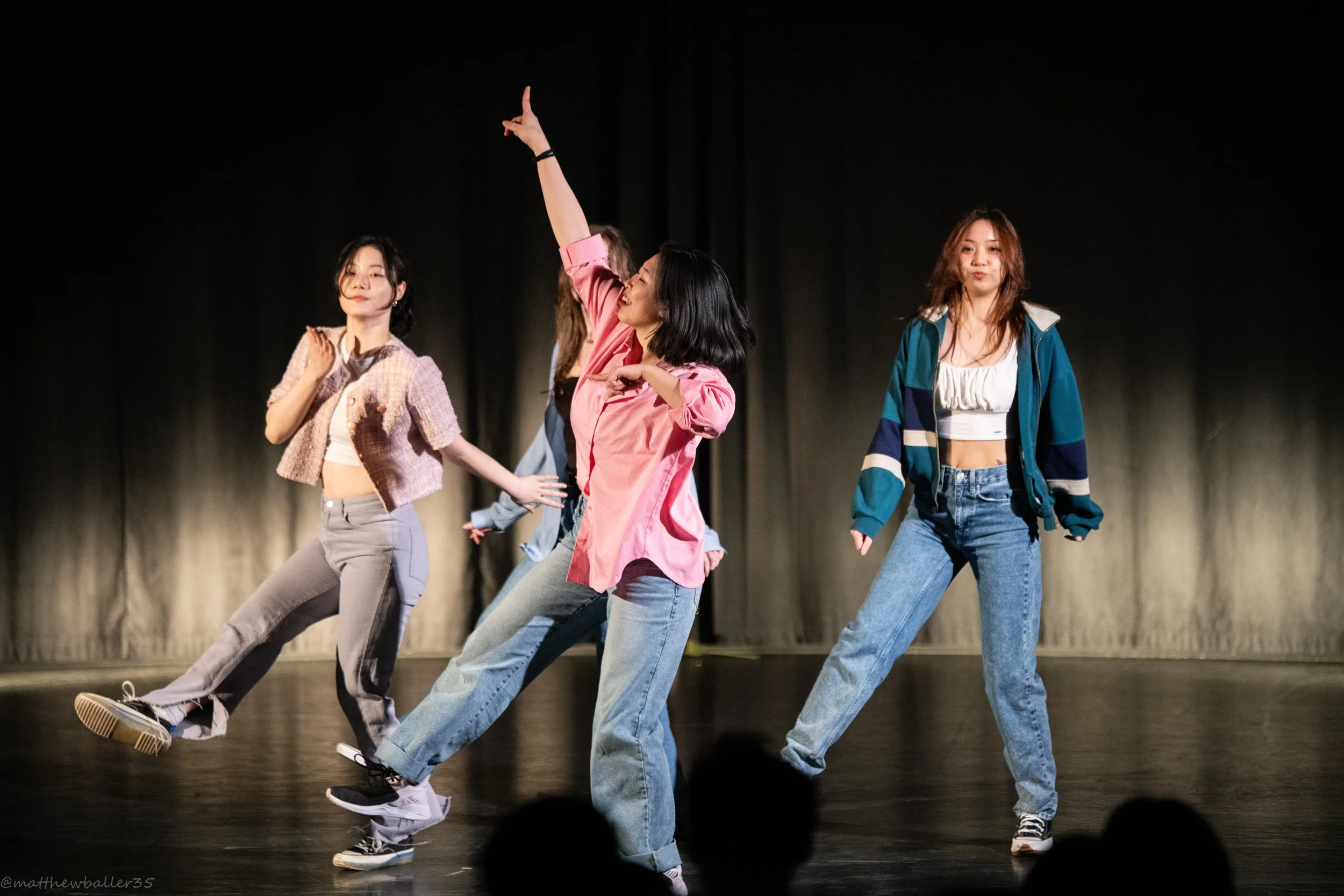 A group of four young women dancing on stage with a black curtain backdrop.