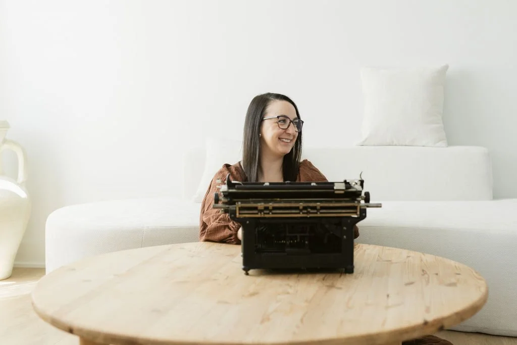 Sarah sitting on the floor, in front of a keyboard looking to the left smiling and thinking about how you should act like you're traditionally publishing when you're self-publishing