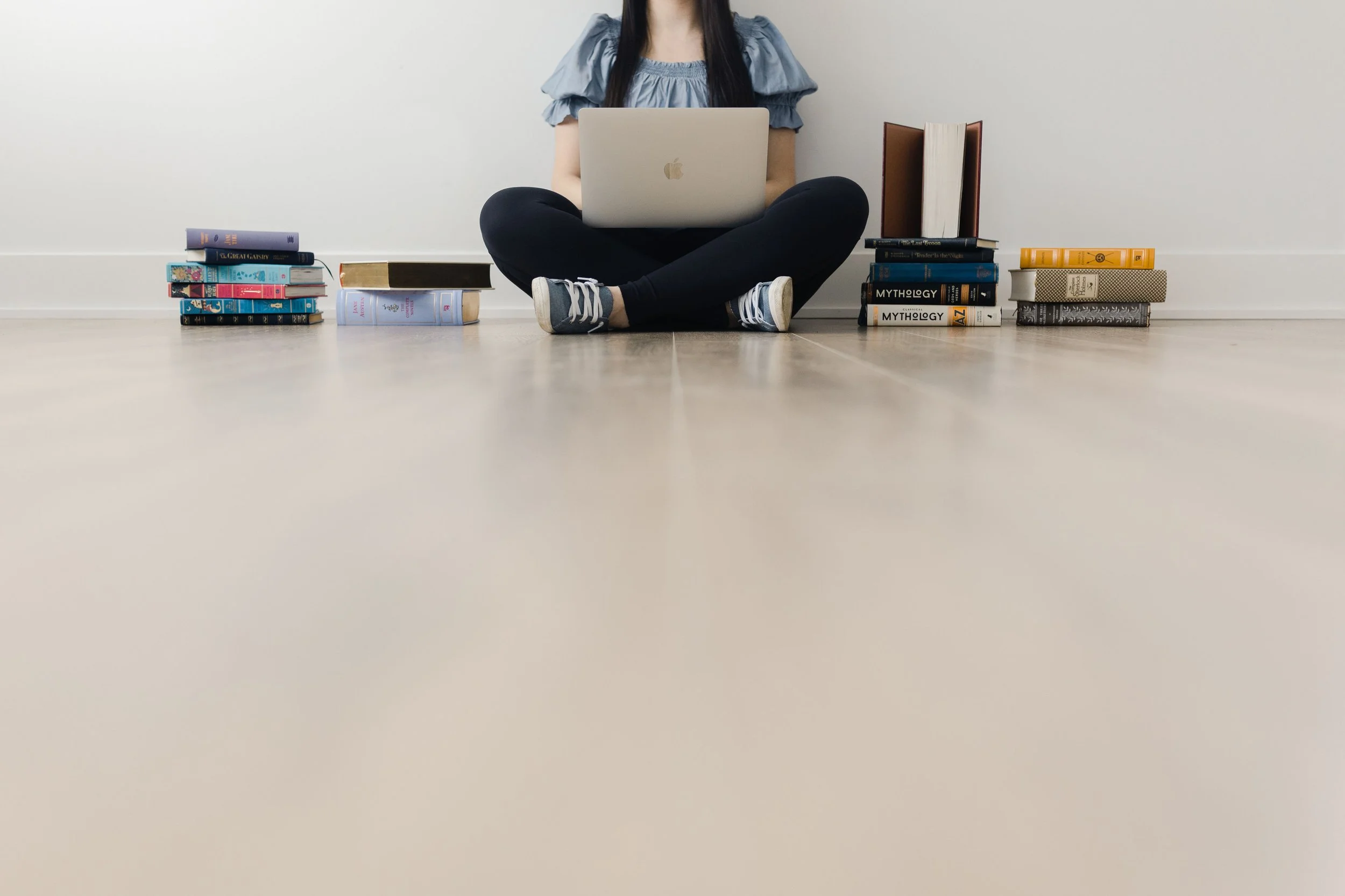 3 digital resources you can create in a day–a woman sitting on the floor surrounded by books, with a laptop on her lap from the shoulders down