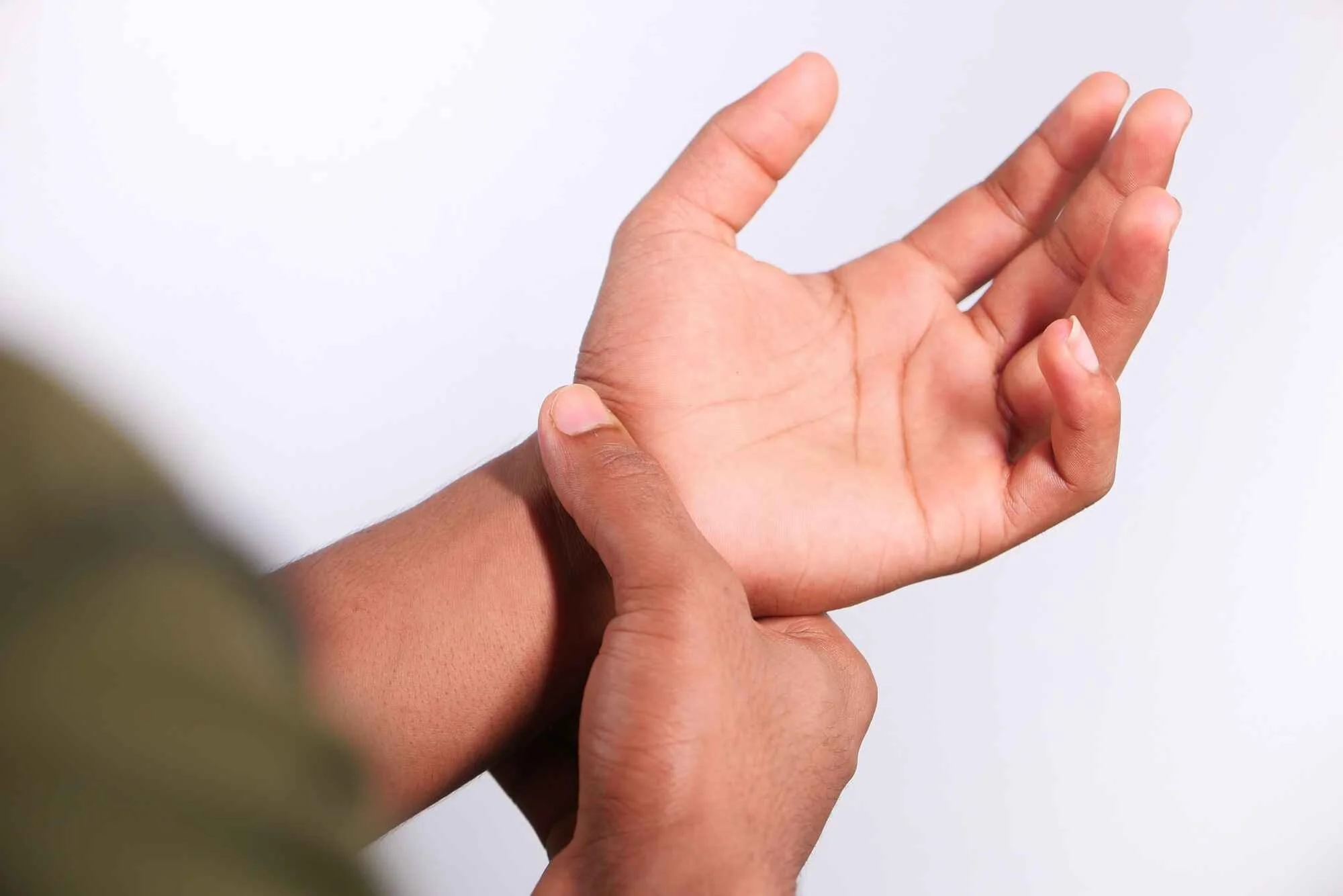 A person demonstrating a hand gesture, with one hand touching the wrist and the other hand with fingers slightly apart.