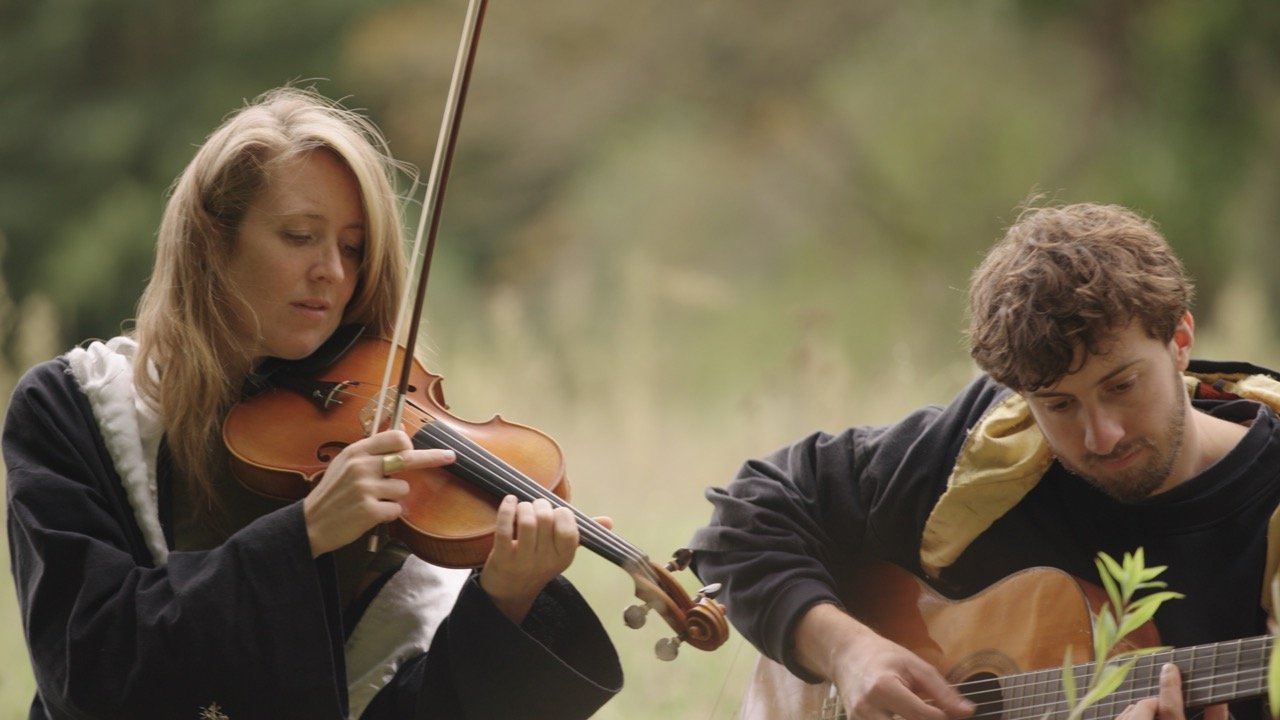 A woman playing the violin and a man playing the guitar outdoors.