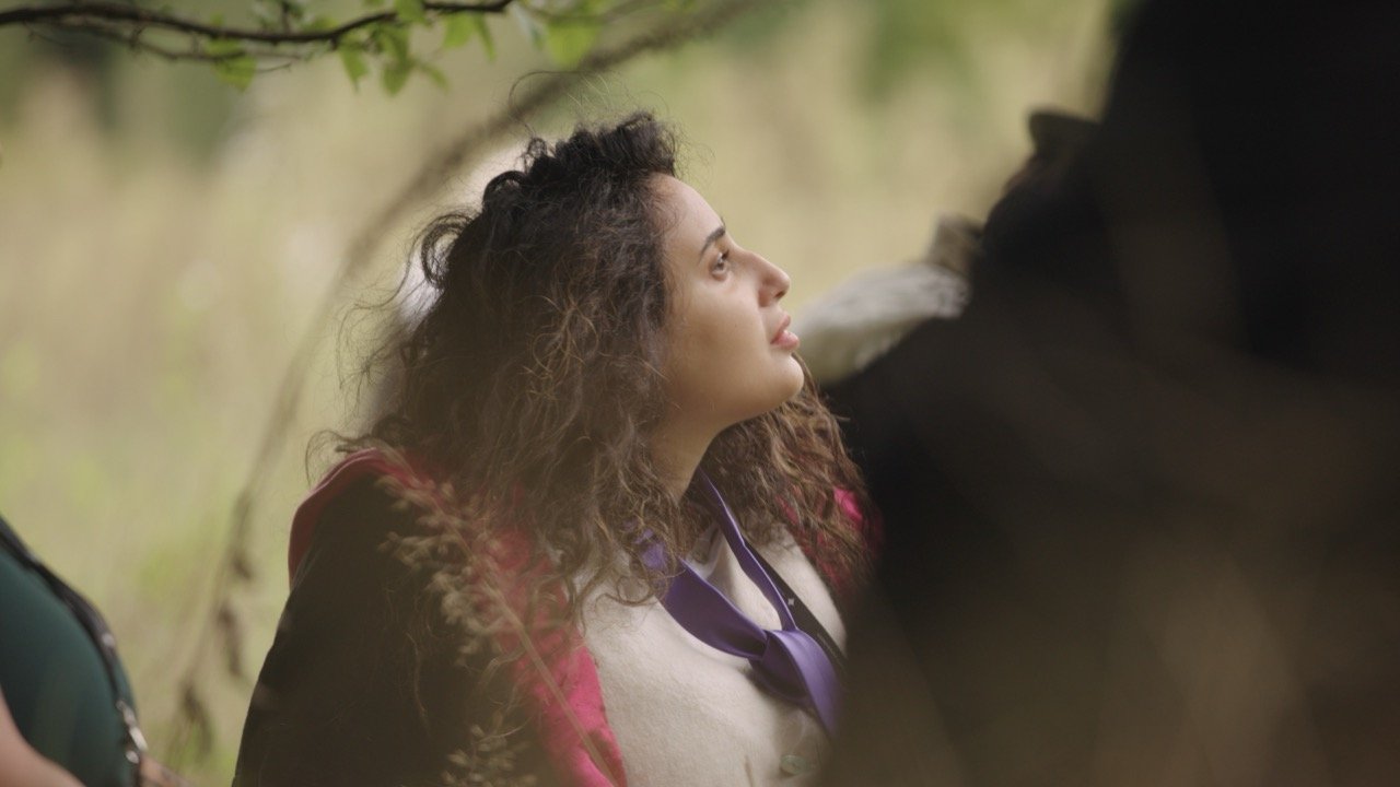 A young girl with curly hair looking upward outdoors with a peaceful expression.