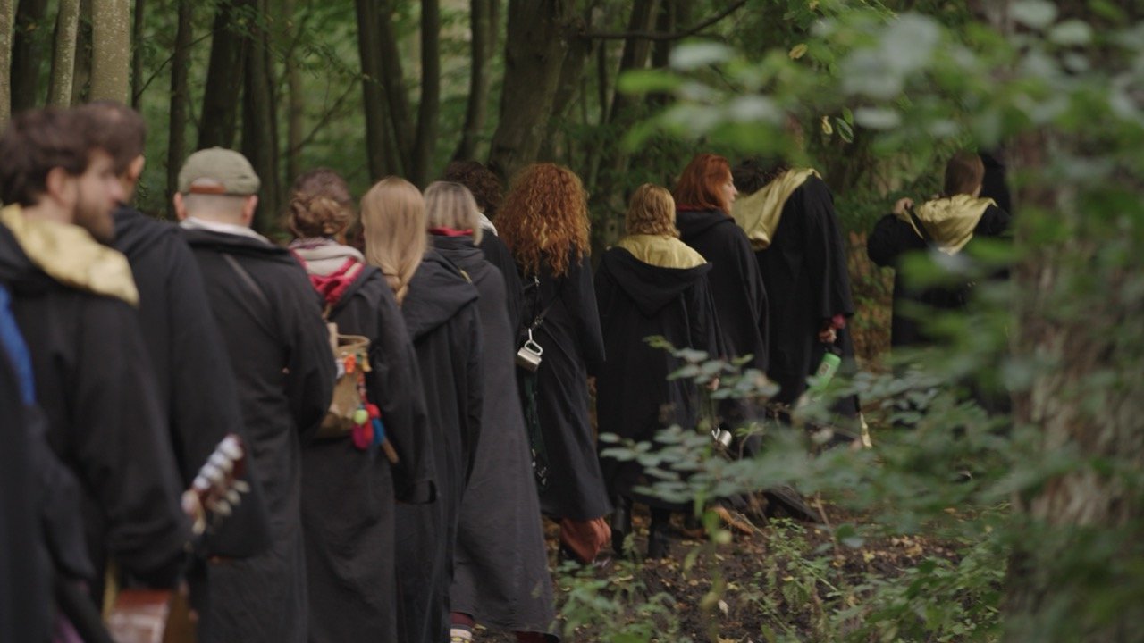 People dressed in black robes walking in a line through a forest.