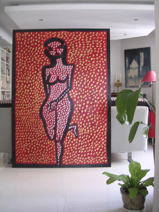 A large framed pop art painting of a woman with short hair, depicted in a dotted pattern with a red background, standing in a modern living room next to a potted plant and white furniture.