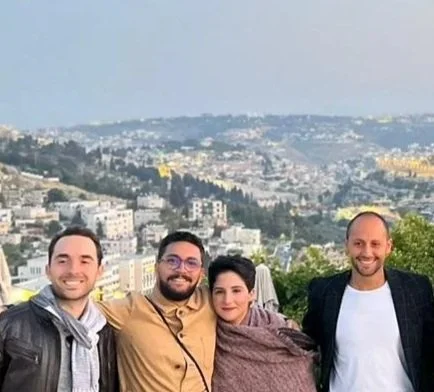 Group of eight people standing together outdoors on a stone wall, with a cityscape and hills in the background at dusk.