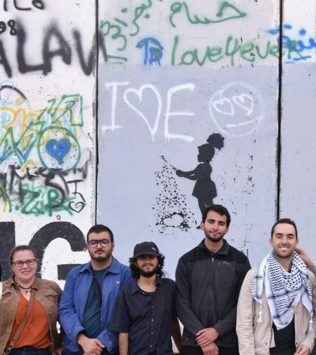 Group of ten people standing in front of a graffiti-covered wall.