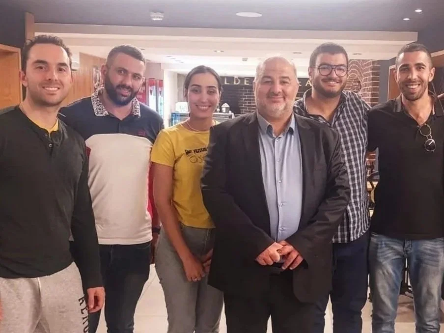 A group of nine people standing together indoors, smiling at the camera.