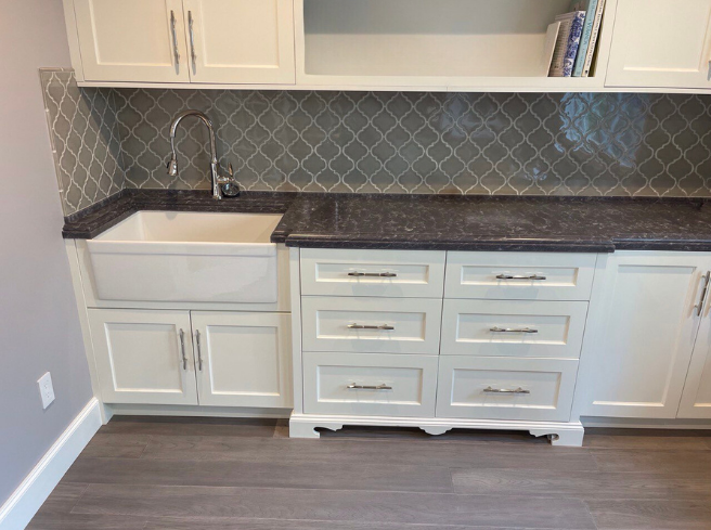 Pantry sink wall with apron-front sink, gray arabesque tile backsplash, shaker drawers, and dark stone countertop with open shelf—Noah & Noble, Greater Seattle.
