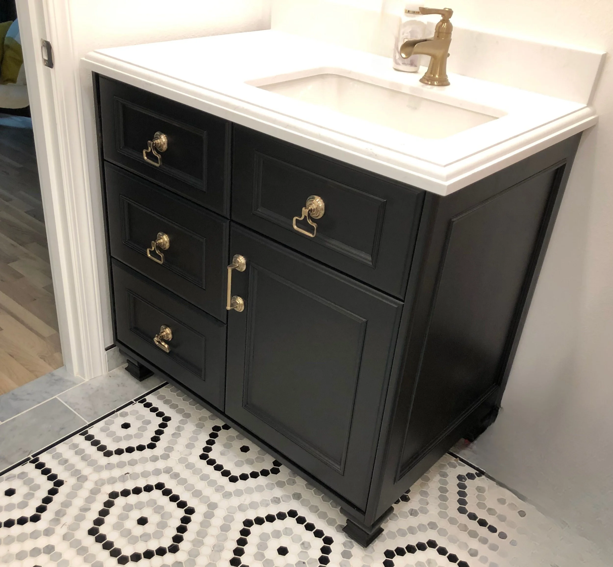 Small-space bathroom vanity in satin black with brass ring pulls and latch, deep storage drawers, and white countertop—custom cabinetry by Noah & Noble.