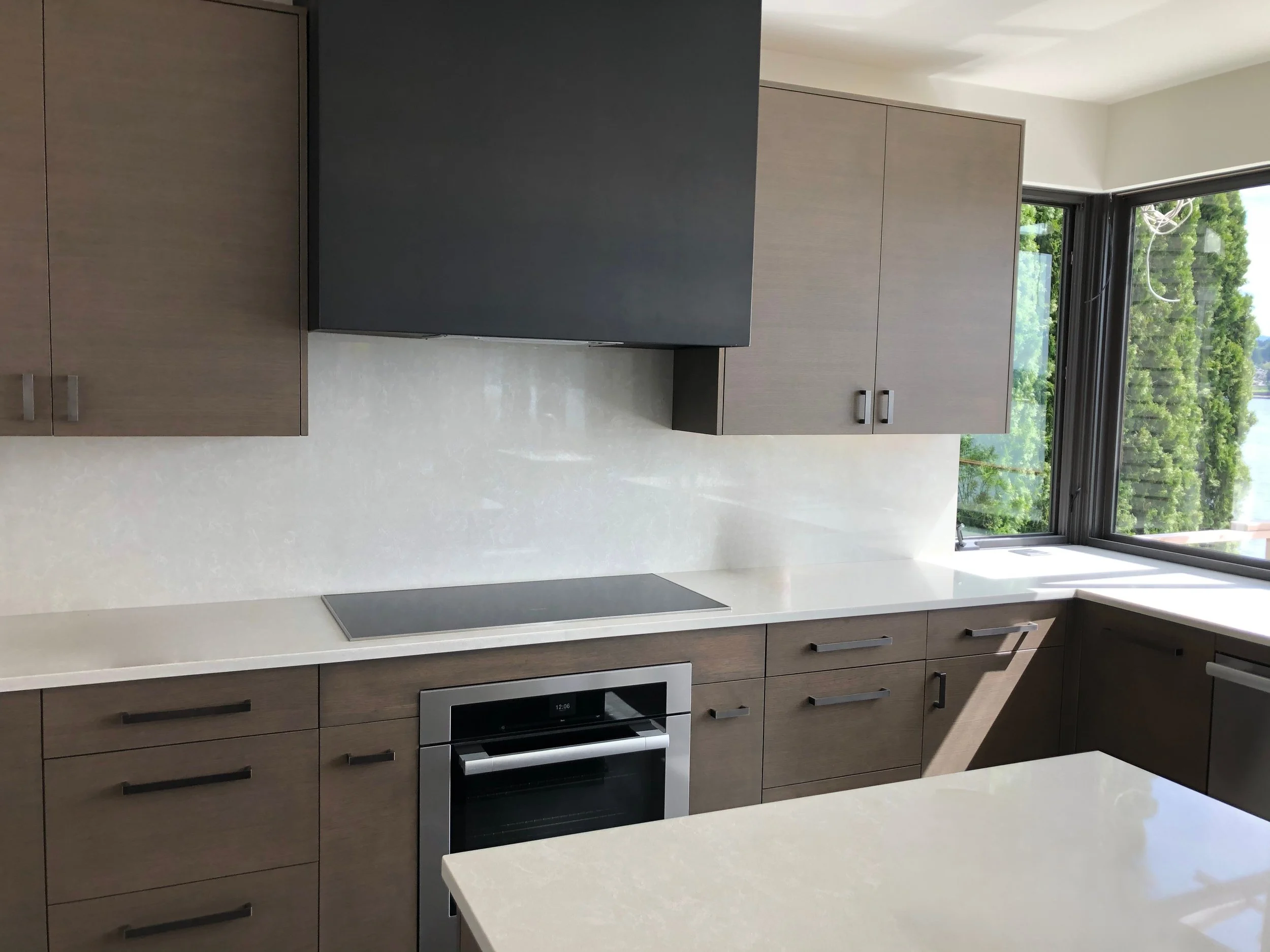 Modern slab-front kitchen in warm wood tones with matte black hood, induction cooktop, and quartz counters—custom cabinets by Noah & Noble.