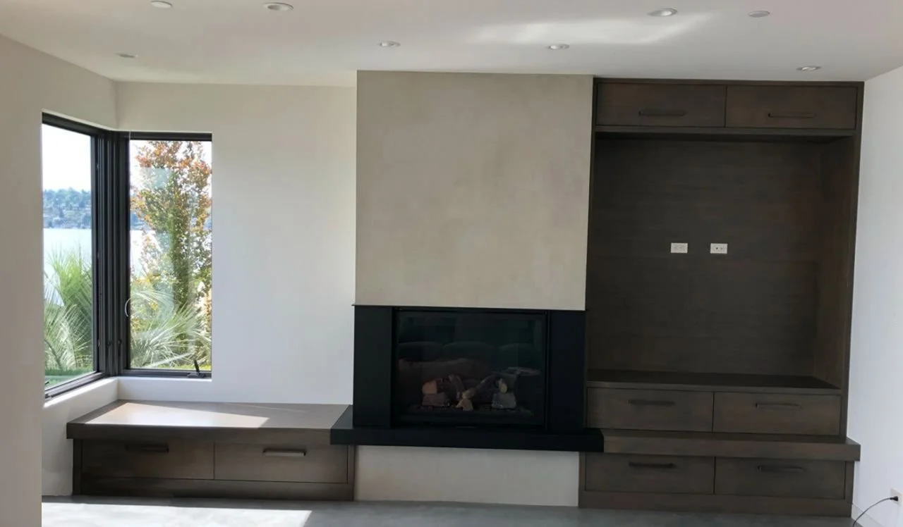 Matching living-room built-ins: fireplace with media niche, bench seating, and drawer storage in warm wood—Noah & Noble.