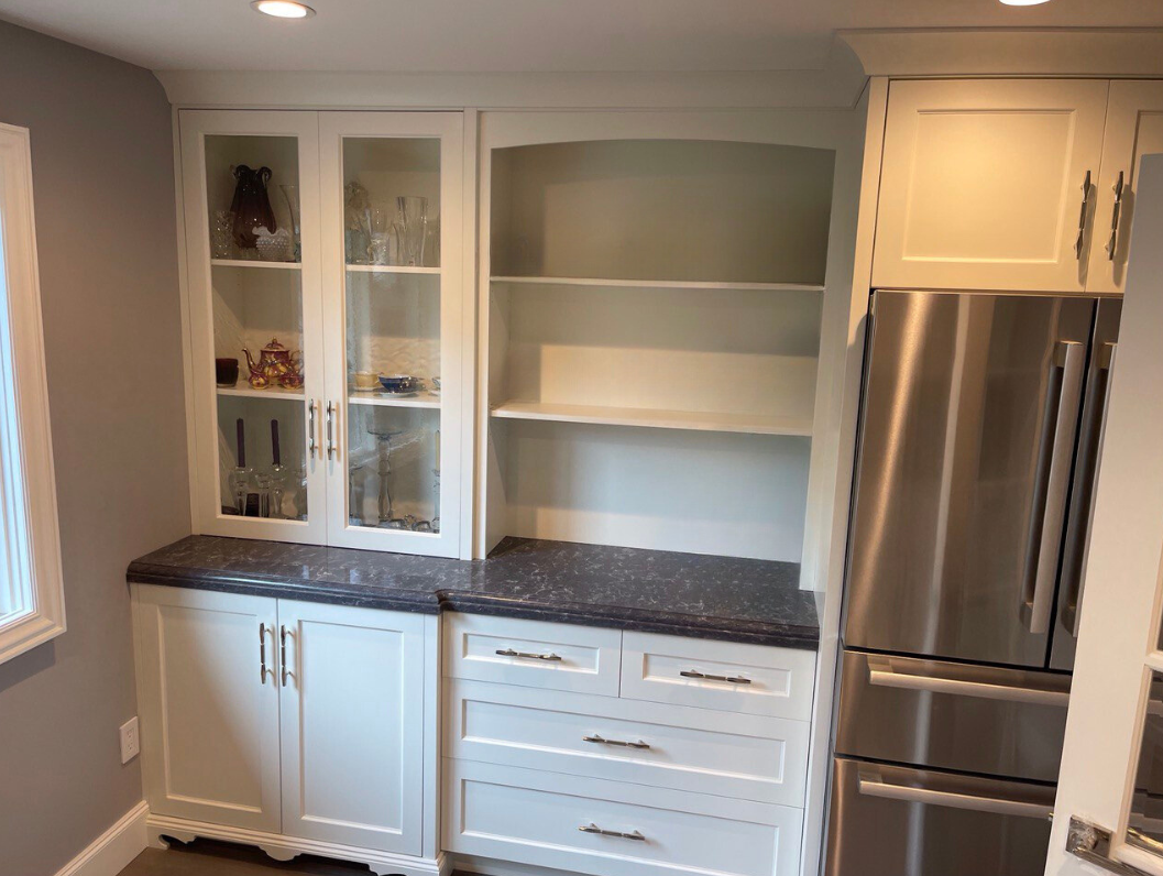 Custom pantry built-ins: white shaker cabinetry with glass doors, deep drawer bank, curved arch shelving, and veined stone countertop—crafted by Noah & Noble.