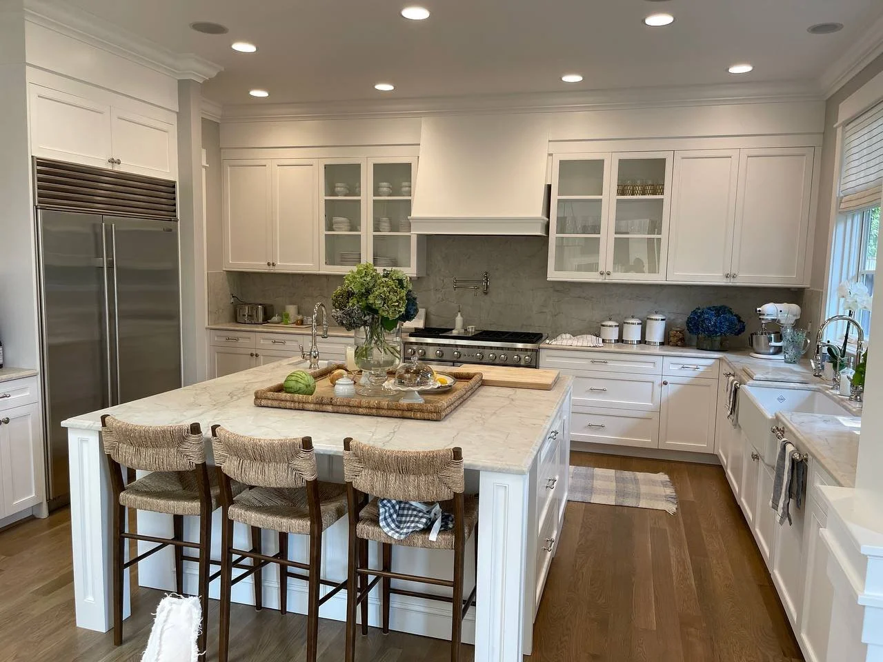 Custom white shaker kitchen cabinets with glass-front uppers, paneled range hood, and large island by Noah & Noble.