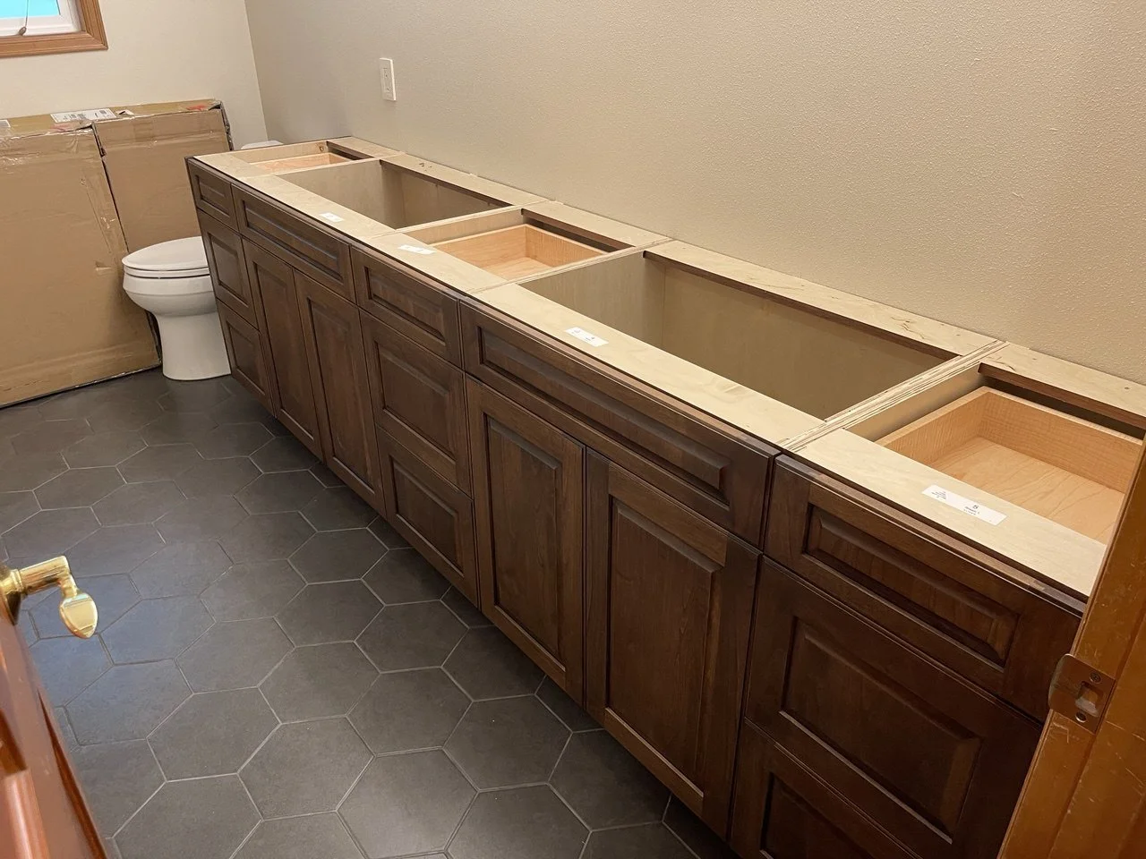 In-progress bathroom vanity: wall-to-wall stained wood cabinets with raised-panel doors, multiple sink bases, and hex tile floor—custom by Noah & Noble, Greater Seattle.