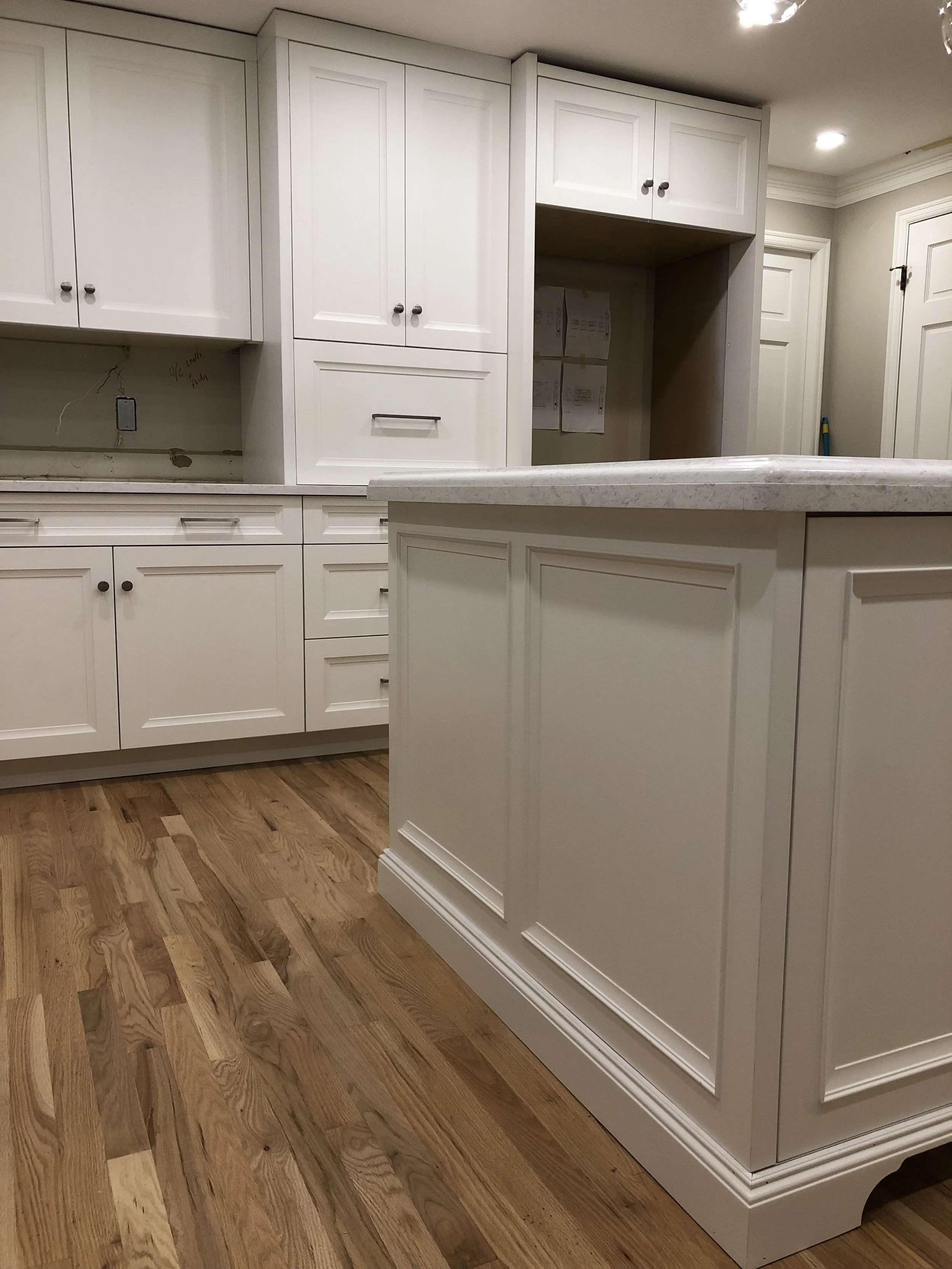 Detail of custom white shaker kitchen—tall pantry/appliance wall with drawer stacks and furniture-style island panel with stone countertop—Noah & Noble, Greater Seattle.