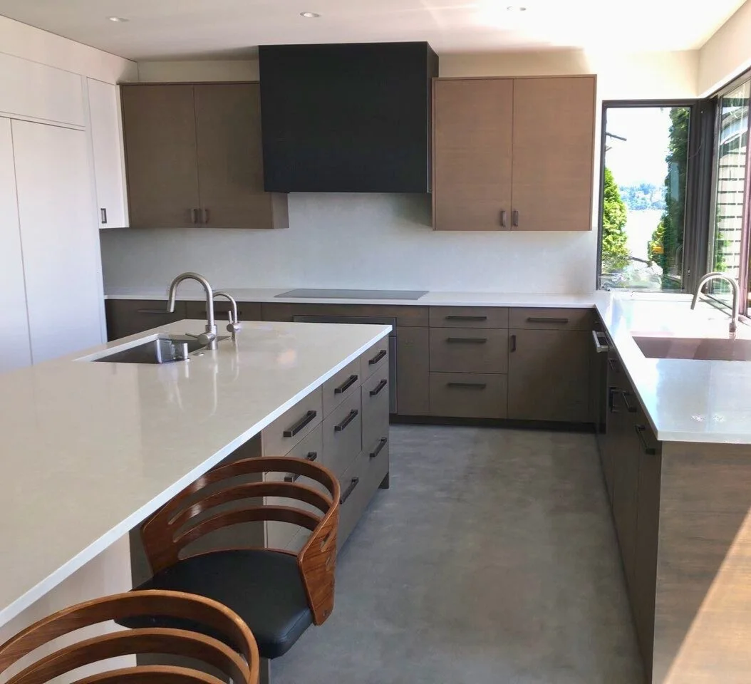 Wide view of U-shaped modern kitchen: slab doors, black hood, long island, and quartz surfaces—Noah & Noble custom cabinets.