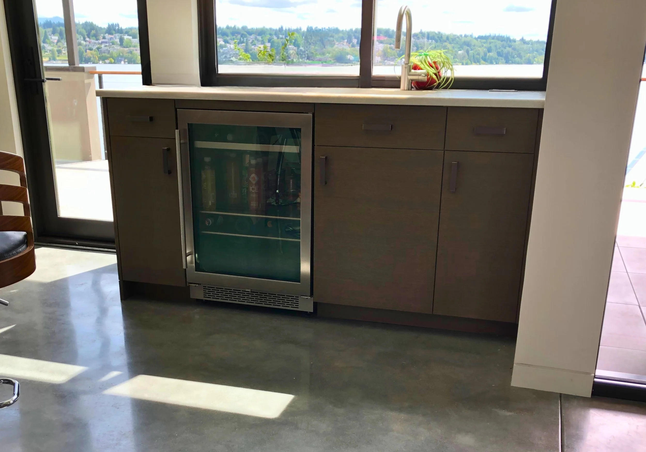 Window wall with undercounter beverage fridge, flat-panel doors, and sleek bar setup—custom cabinetry by Noah & Noble.
