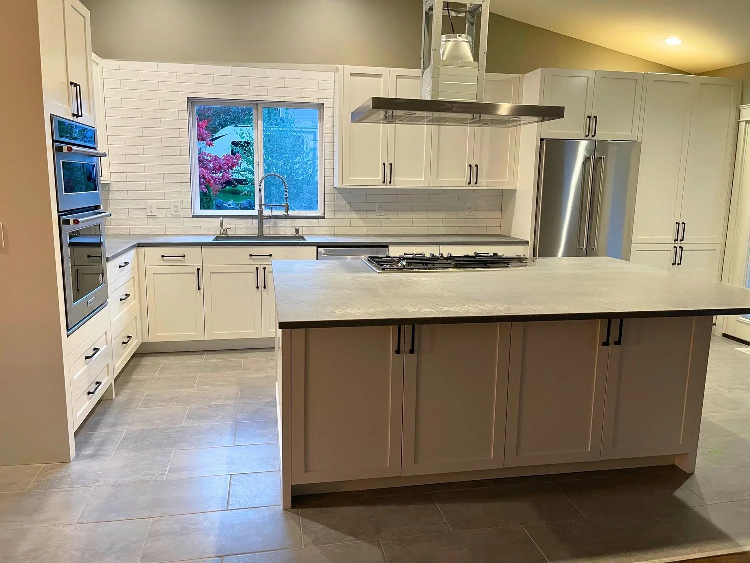 Custom shaker cabinetry with black hardware, big prep island, and stainless appliances against a white subway backsplash—Noah & Noble custom kitchen.