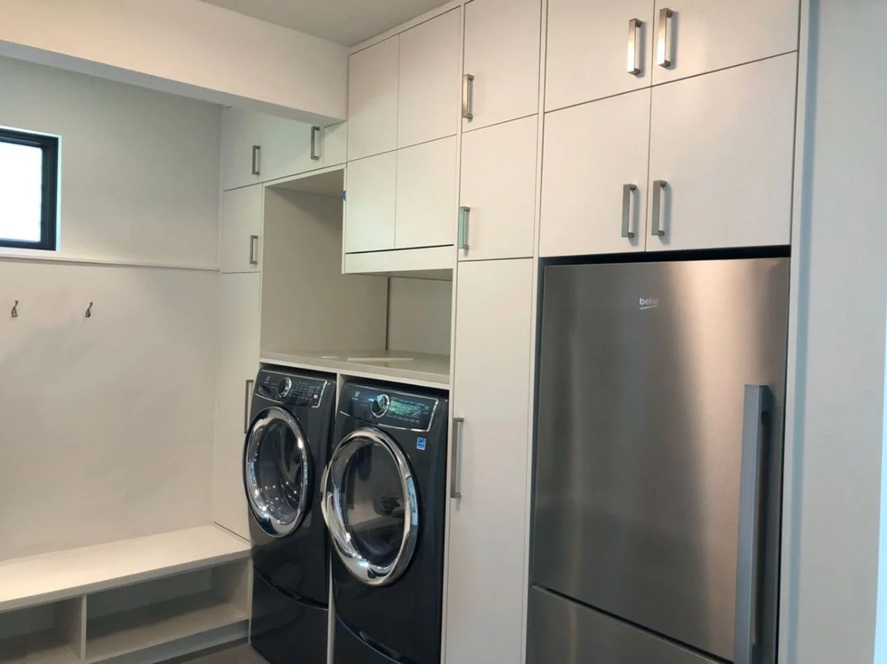 Custom laundry/mudroom cabinets with slab fronts, bench with cubbies, folding counter over front-load washer/dryer, and built-in refrigerator—Noah & Noble, Greater Seattle.