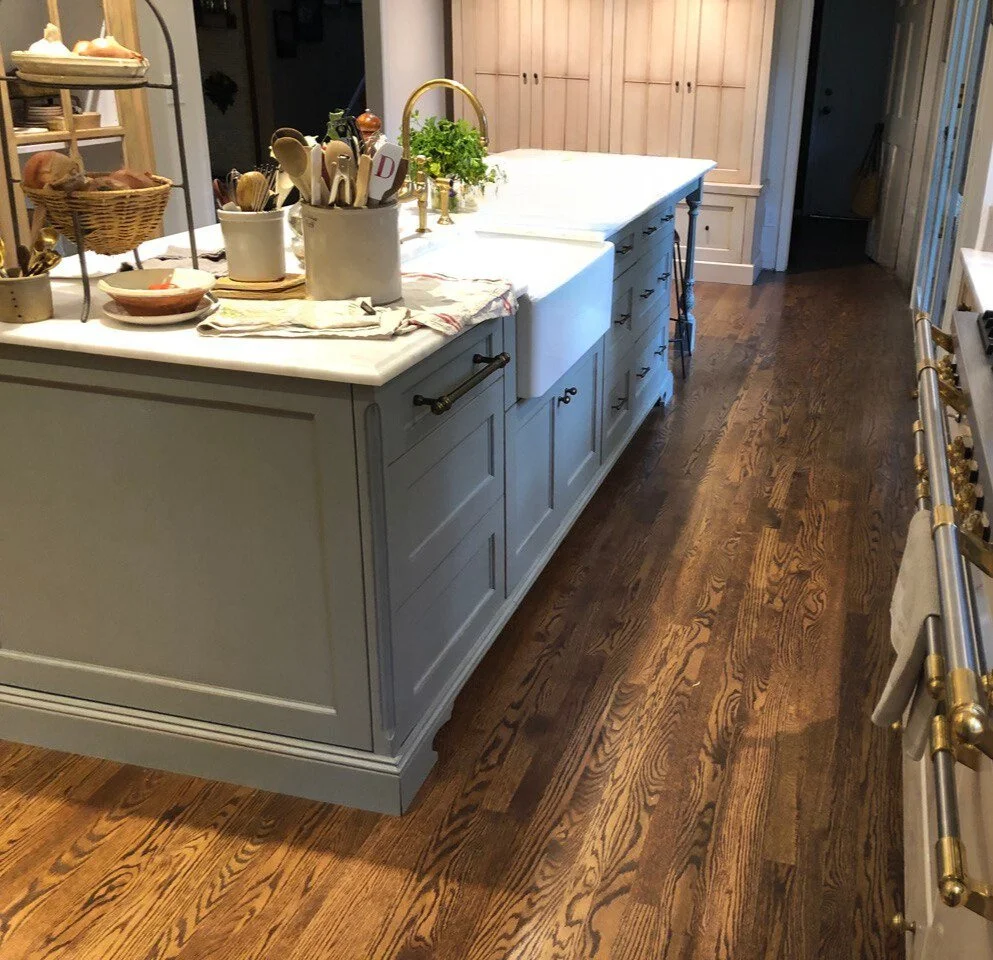 Apron-front farmhouse sink set in a white marble island with blue-gray shaker cabinetry and brass bridge faucet—Noah & Noble, Greater Seattle.