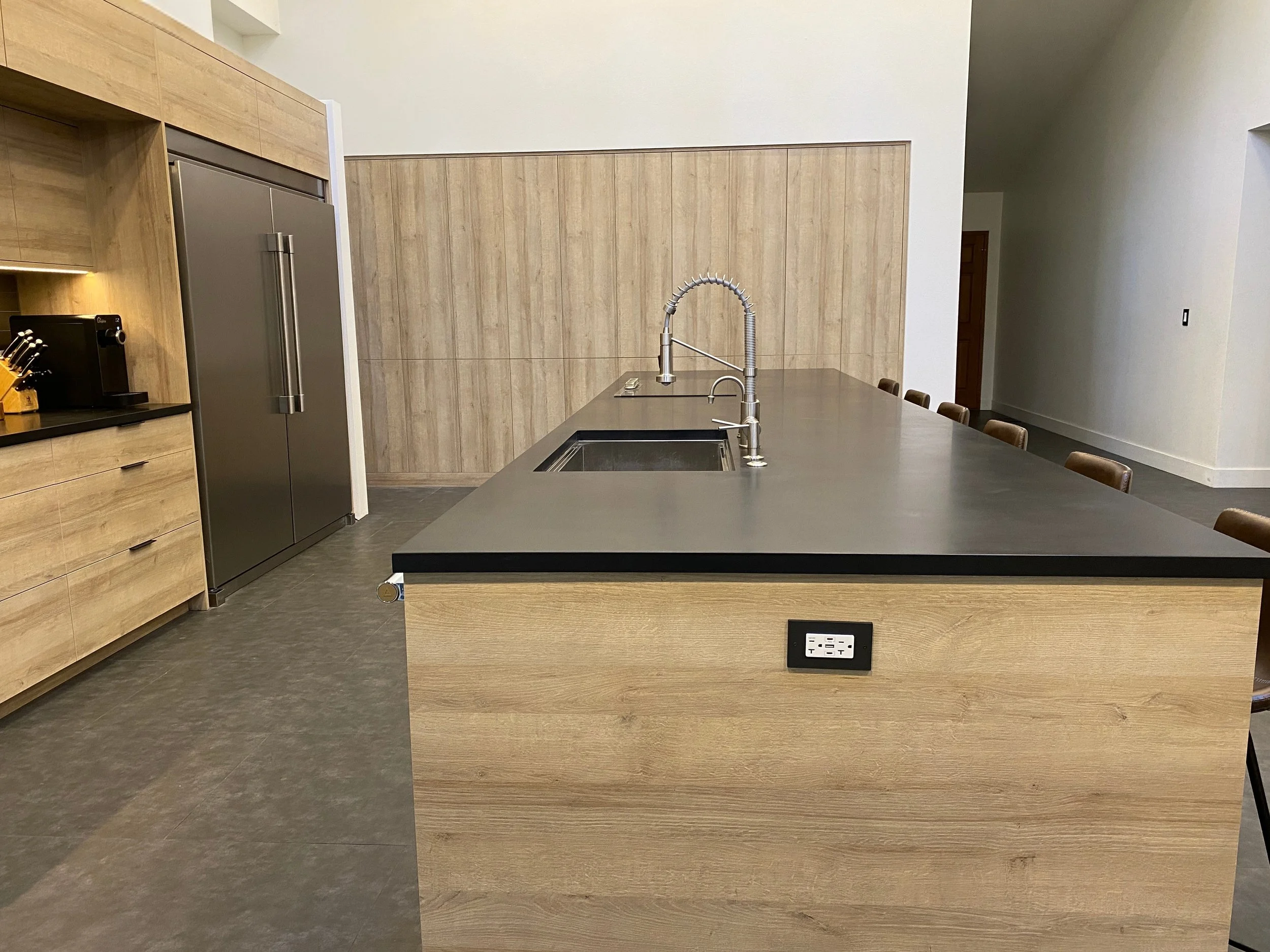 Island sink with commercial-style faucet opposite a built-in refrigerator wall and matching wood cladding—Noah & Noble custom kitchen.