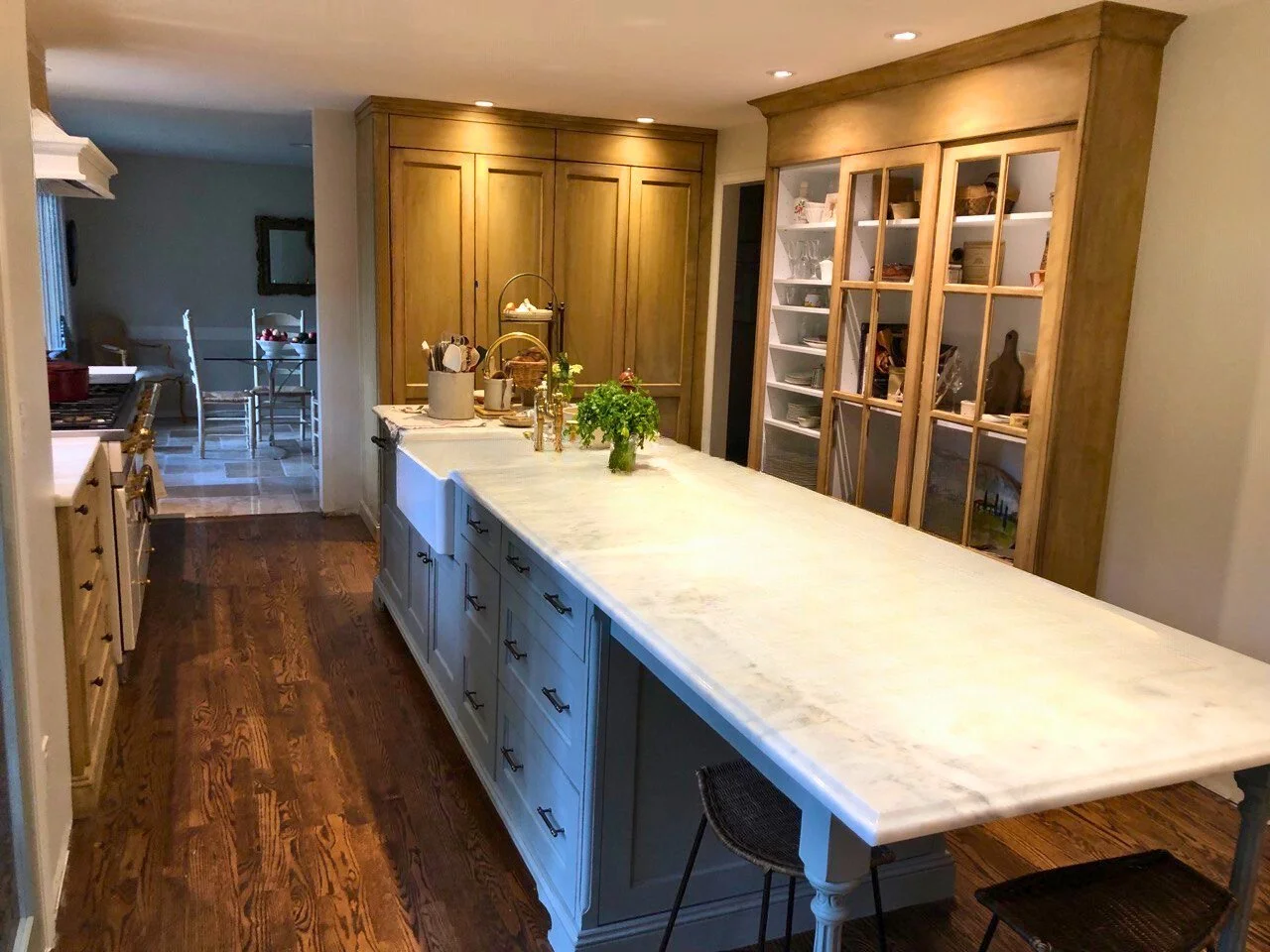 Classic kitchen with white marble island, blue-gray shaker base, apron-front sink, and tall stained pantry + glass-mullion hutch—Noah & Noble, Greater Seattle.