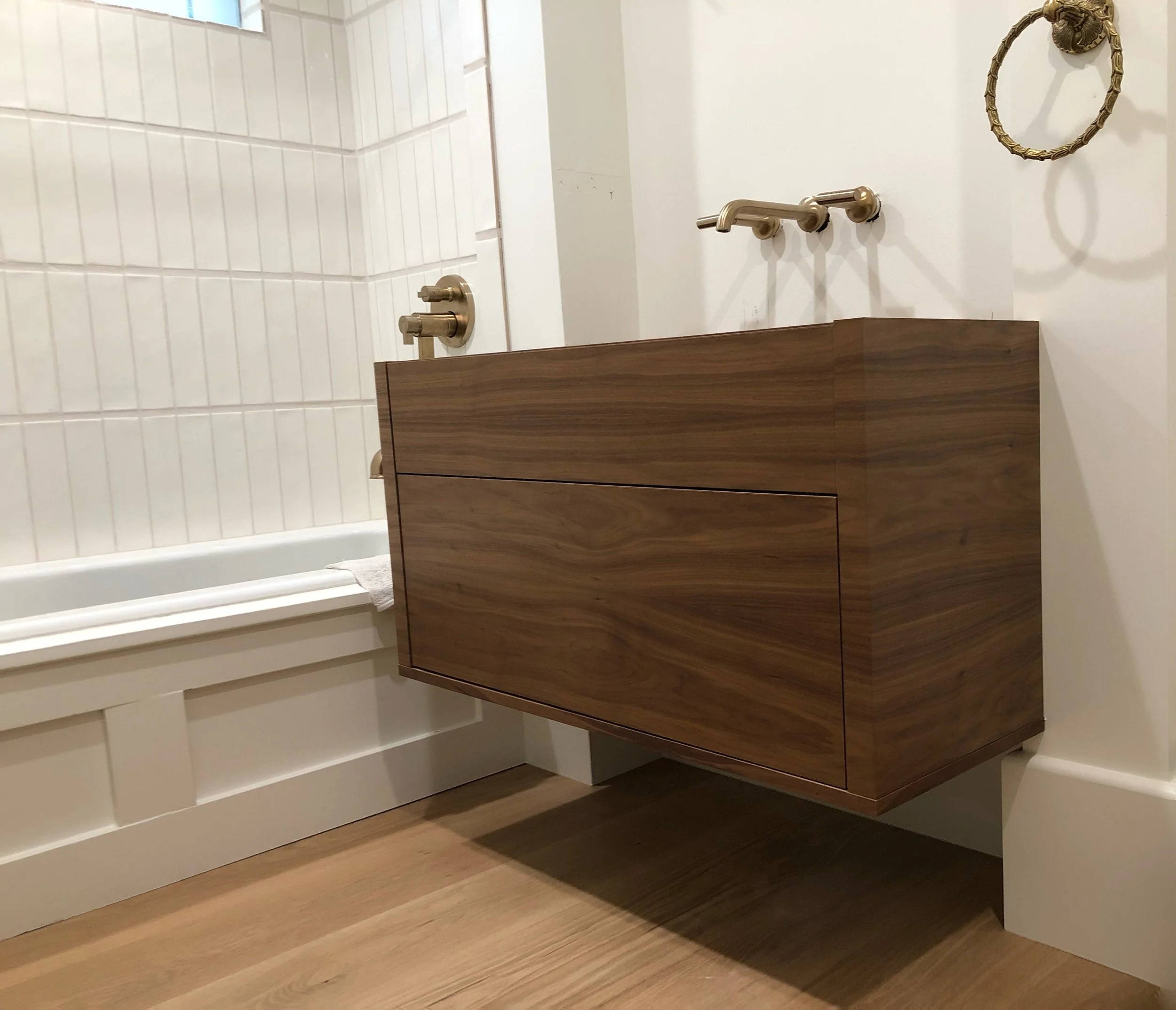 Floating walnut bathroom vanity with slab-front drawer and wall-mounted brass faucet—custom build by Noah & Noble, Greater Seattle.
