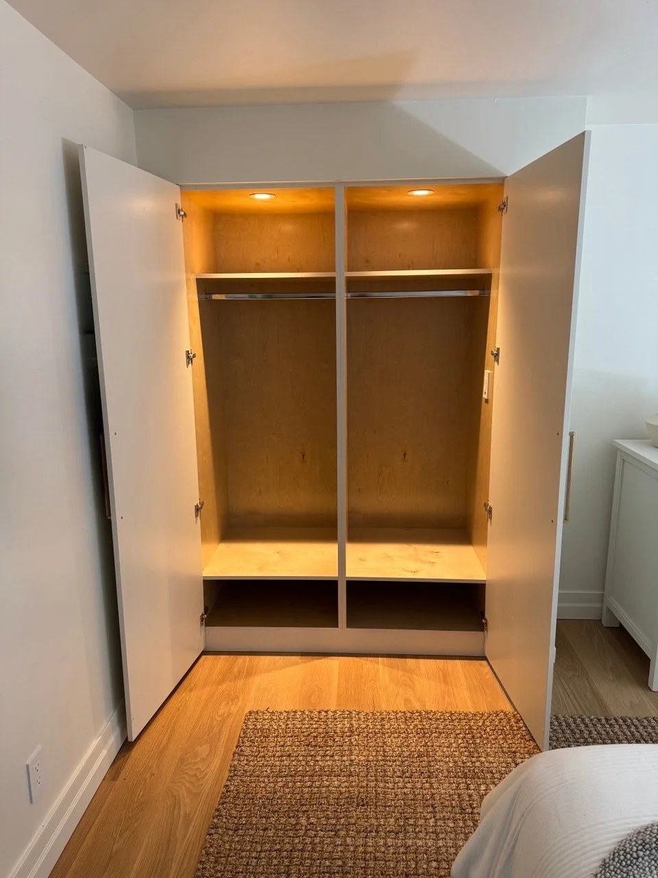 Interior of custom bedroom closet with warm wood interior, integrated lights, double hanging rod, upper shelf, and shoe cubbies—Noah & Noble.