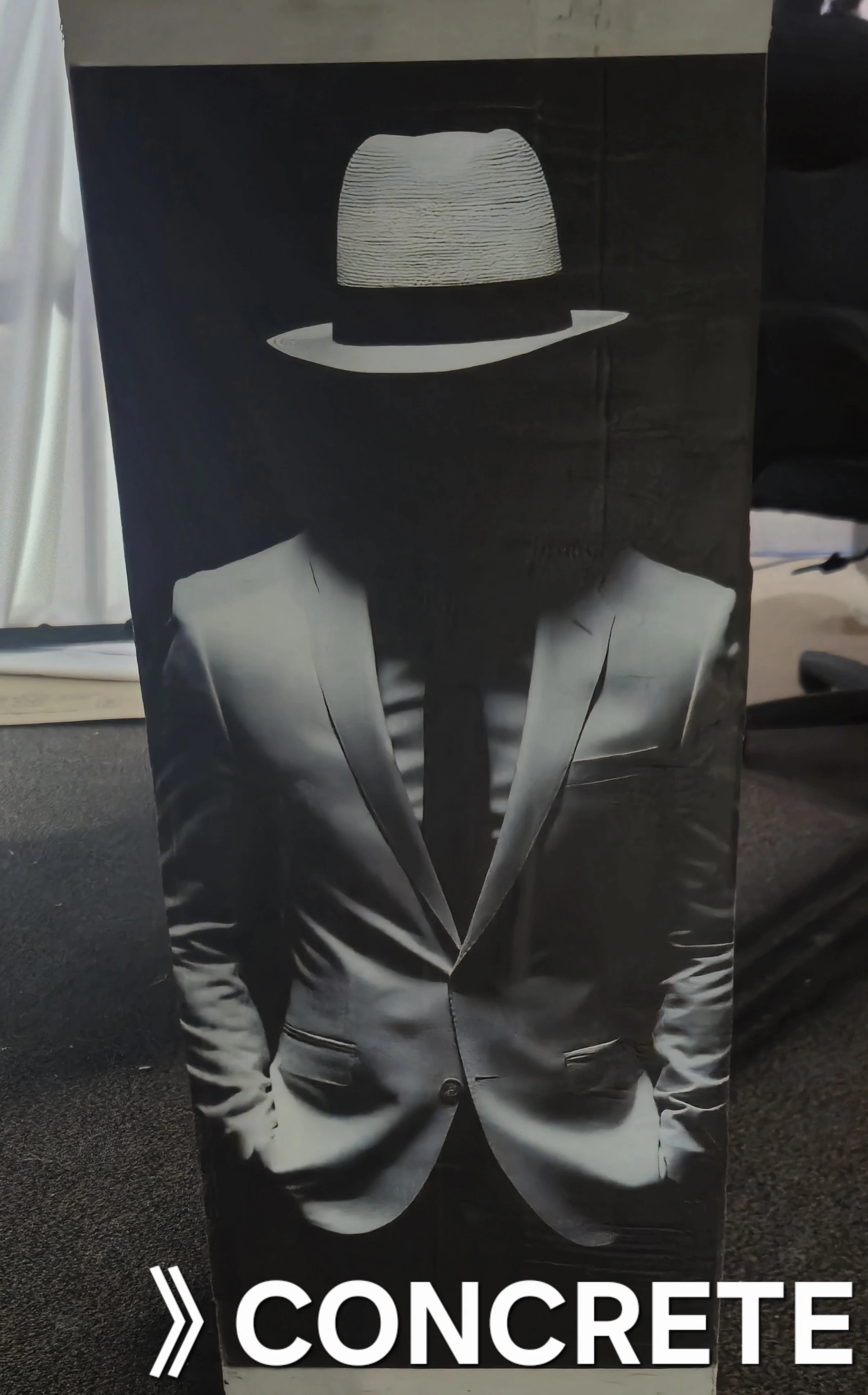 Black and white box featuring a person in a suit with hands in pockets, wearing a fedora hat. The word 'CONCRETE' is written at the bottom.