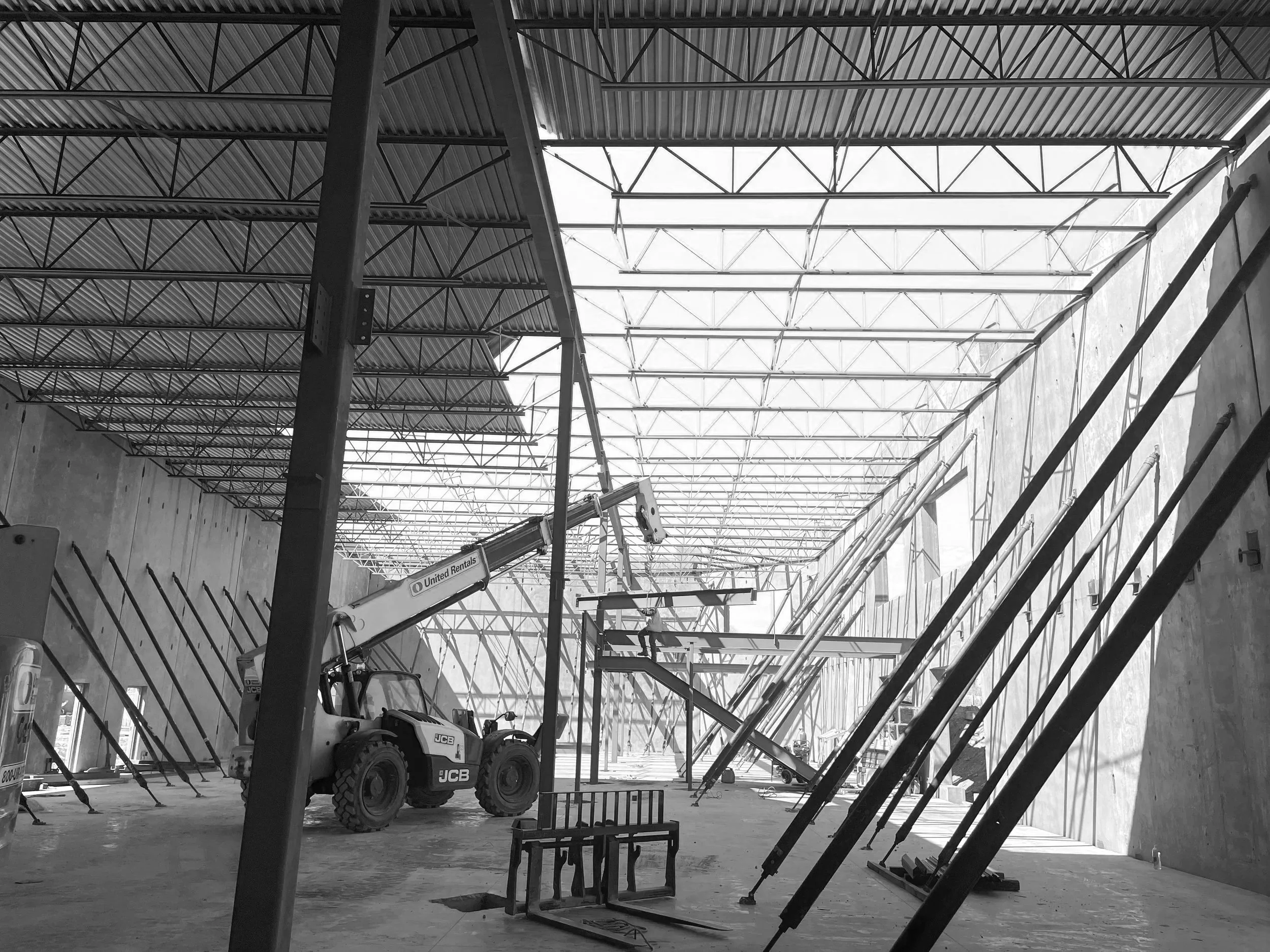 Construction site inside a large building with steel supports, a telescopic lift, and scaffolding, indicating ongoing construction work.