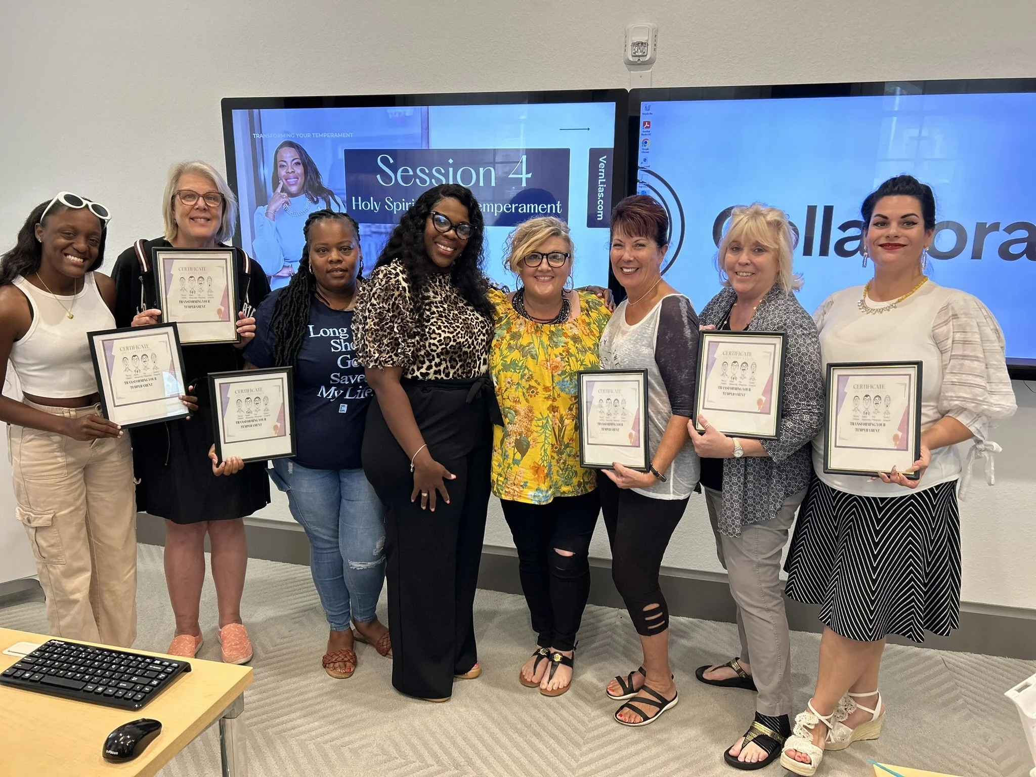 Group of nine women standing together in a room, some holding certificates, posing for a photo during a workshop or seminar with a presentation screen behind them displaying 'Session 4' and 'Holy Spirit Temperament.'