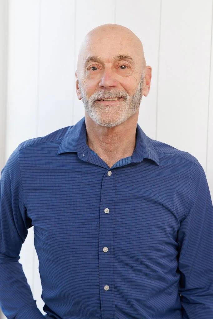 Bald man with a goatee smiling against a textured background.