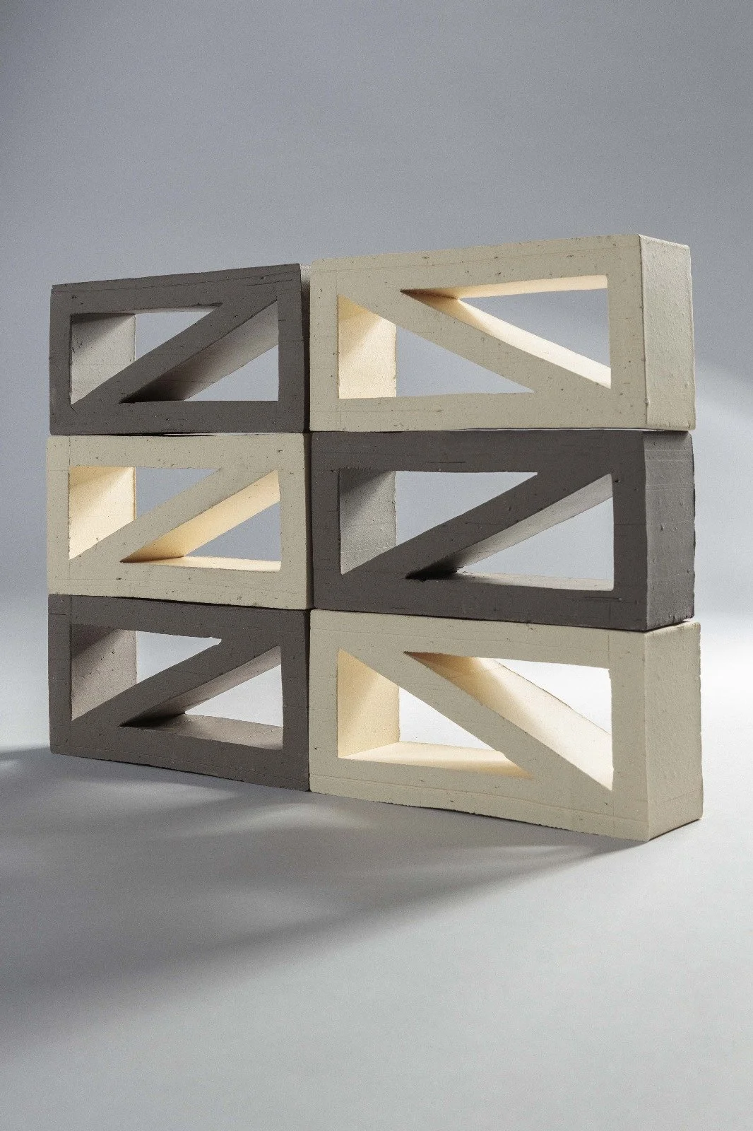Stacked white and gray concrete blocks with diagonal cutouts, arranged in two columns and three rows, against a plain light background.