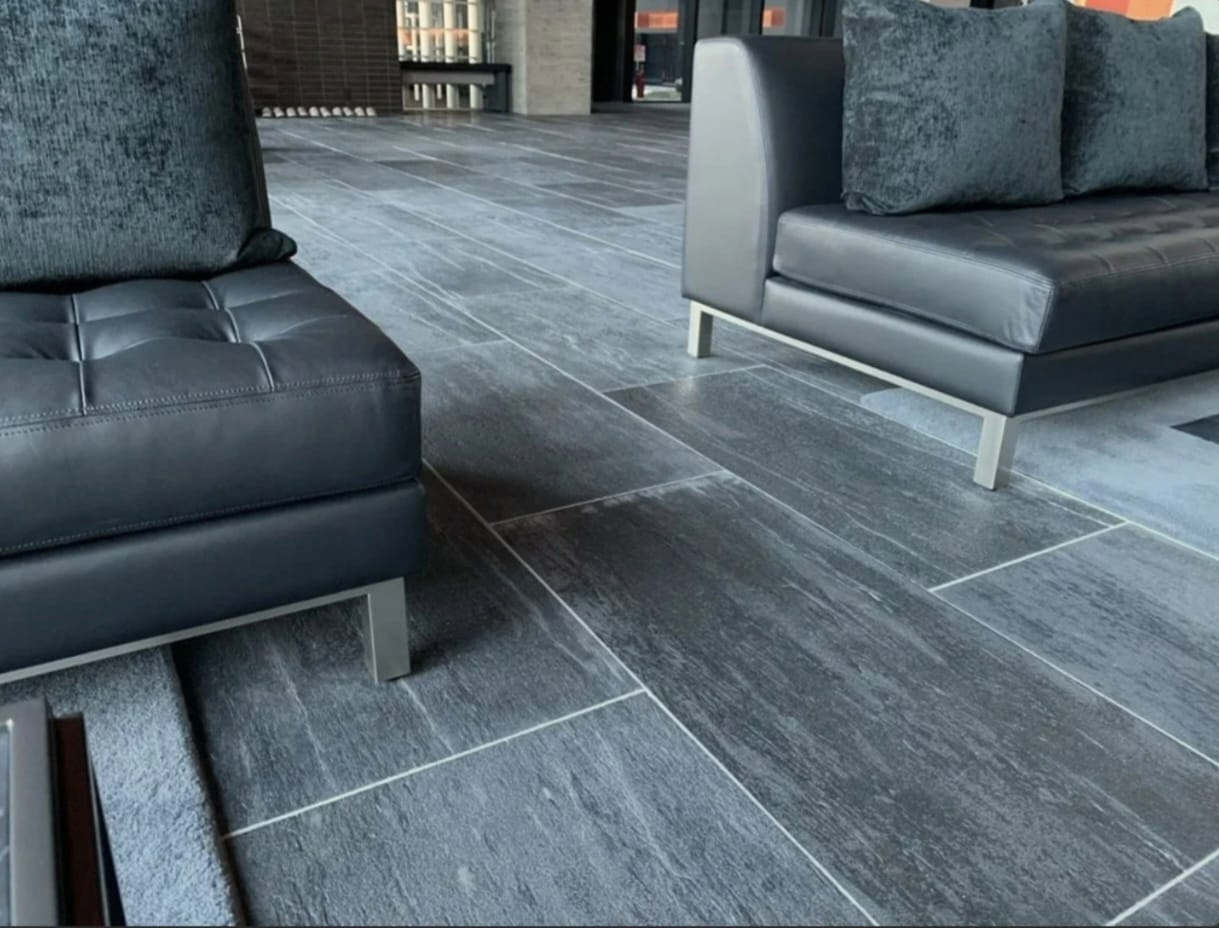 Modern lounge area with black leather sofas and dark gray tiled floor.