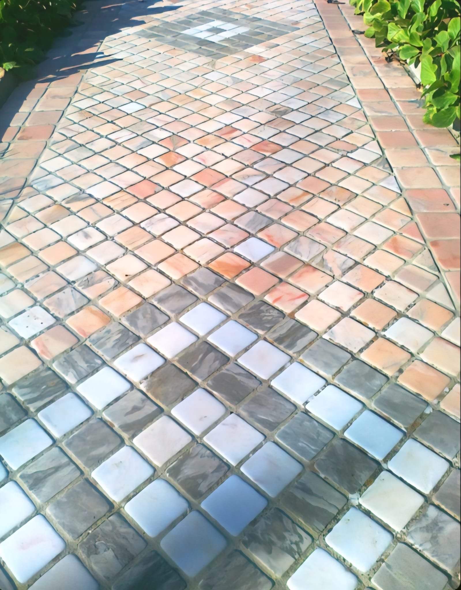 Colorful tiled walkway with pavers arranged in a pattern, bordered by greenery on the sides.