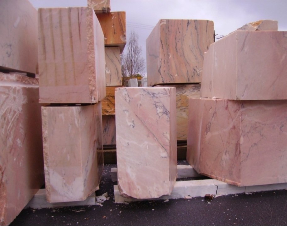 Large pink and beige marble blocks stacked outdoors with trees in the background.