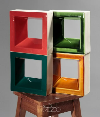 Colorful geometric sculptures on a wooden stool, including red, green, teal, and orange cube frames with hollow centers.