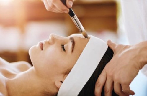 A woman receiving a facial treatment with a brush on her forehead in a spa setting.