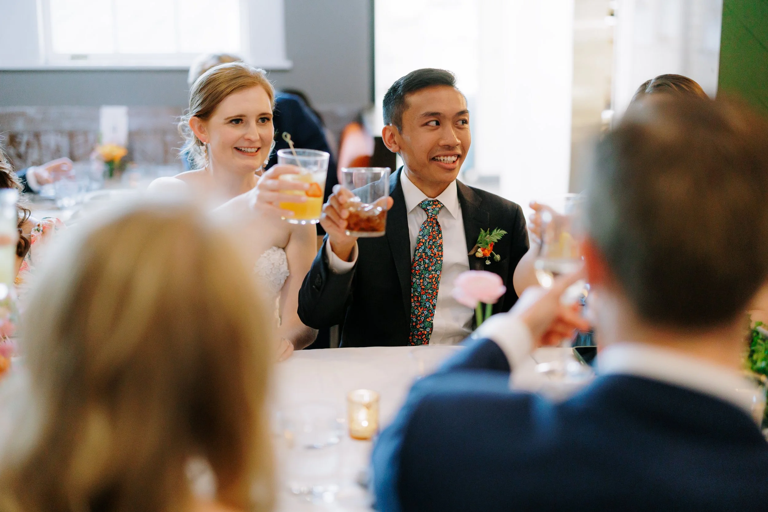 People celebrating at a wedding reception, raising glasses for toast, with a bride and groom in focus.