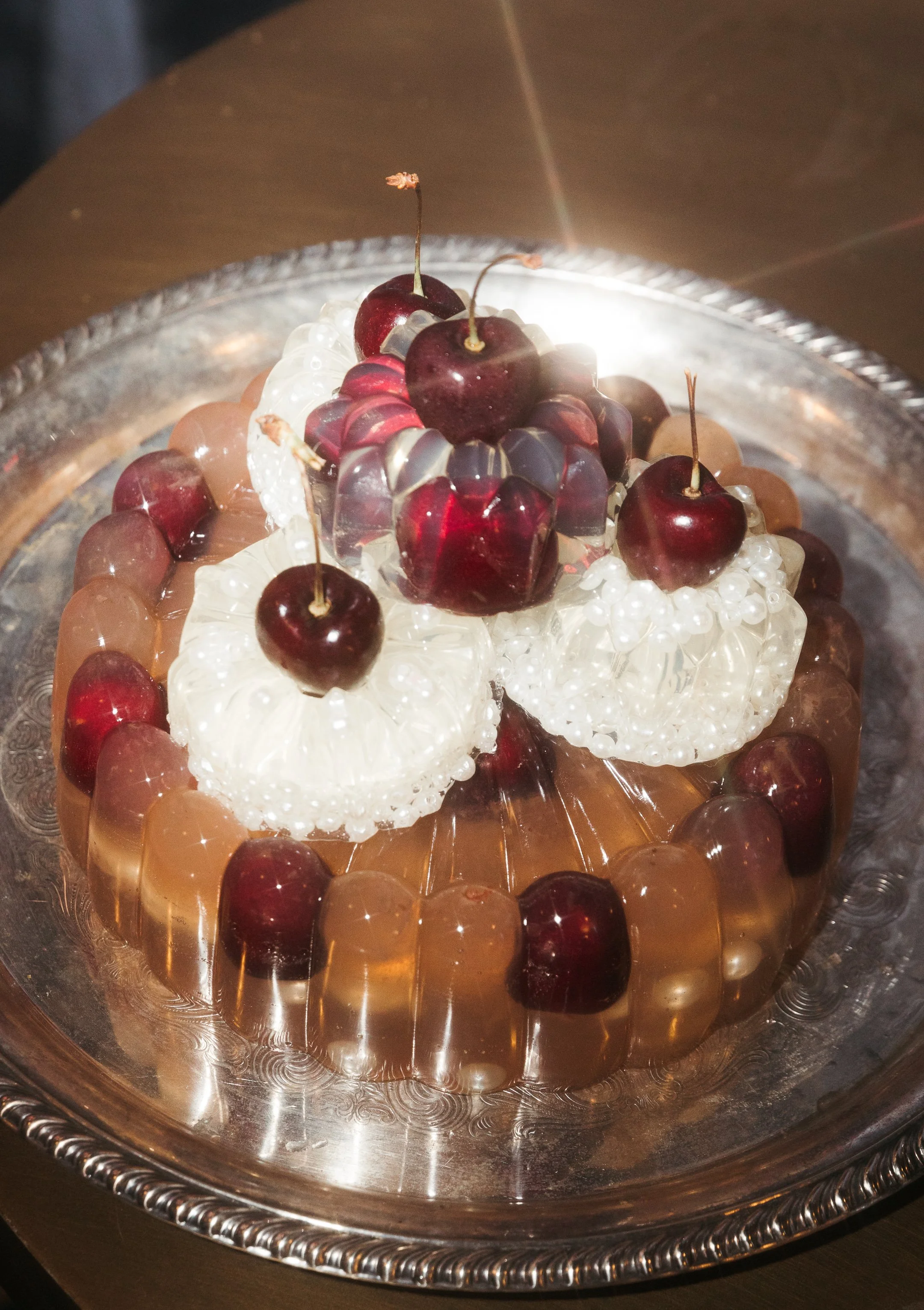 A decorative fruit display on a silver tray featuring cherries, white pearls, and grape-like candies arranged in a circular pattern.