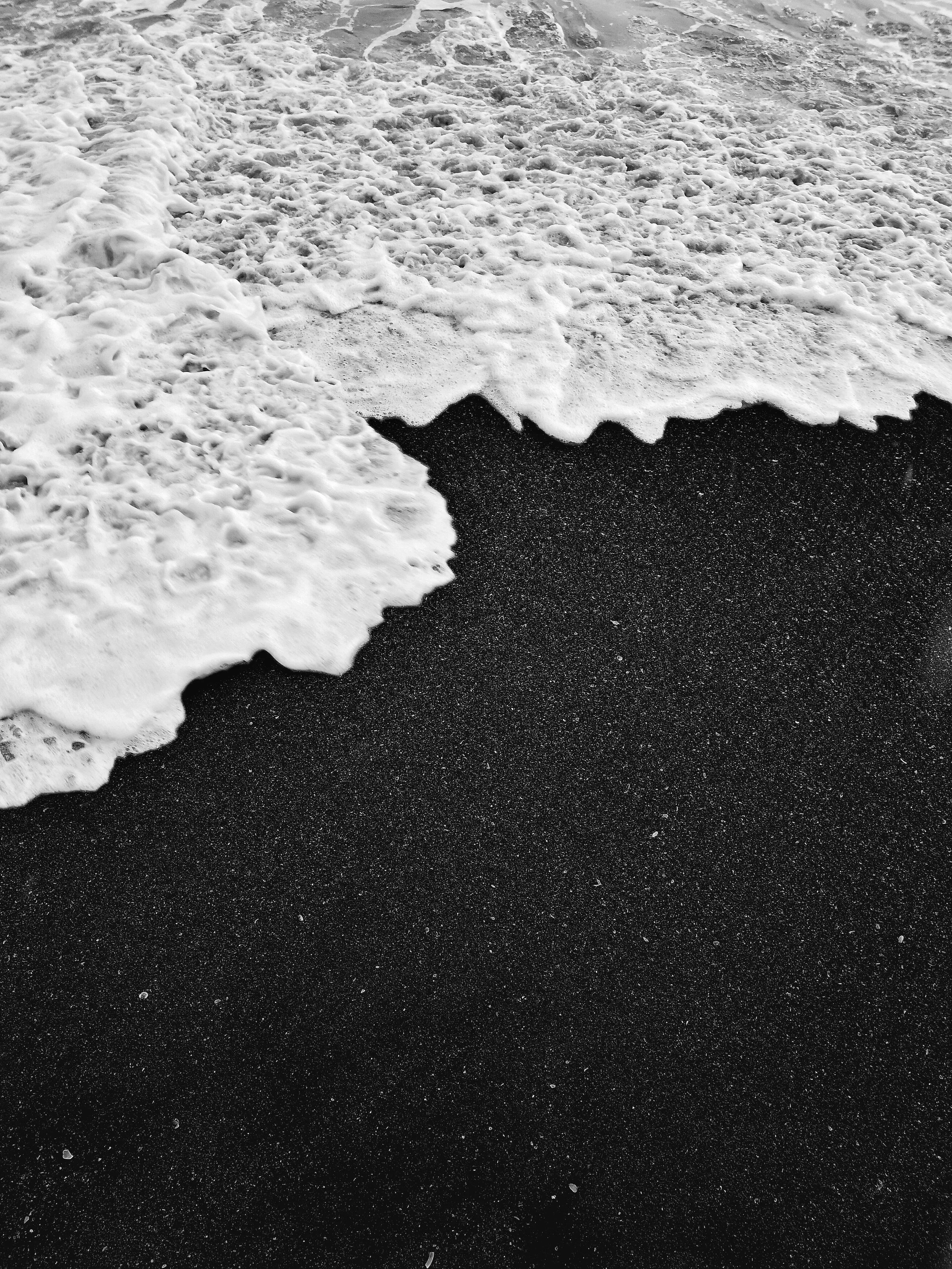 Close-up of black sandy beach with white foamy ocean waves washing ashore.
