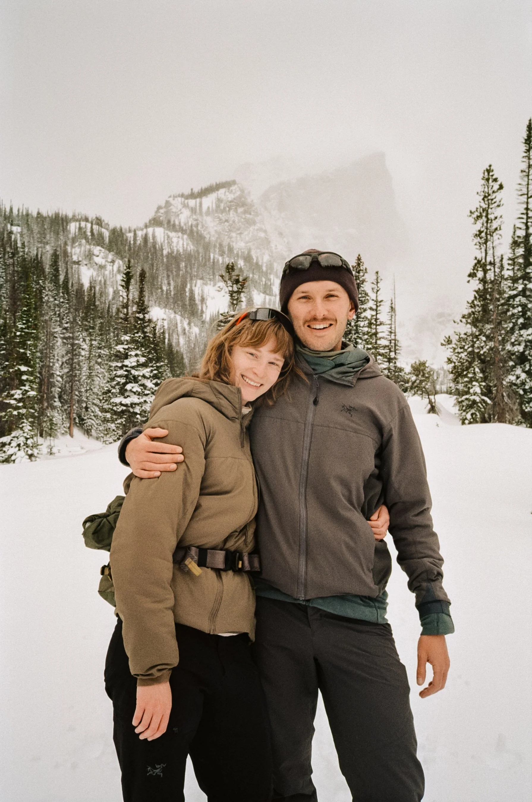husband and wife hugging for a photo with a snow mountain backdrop