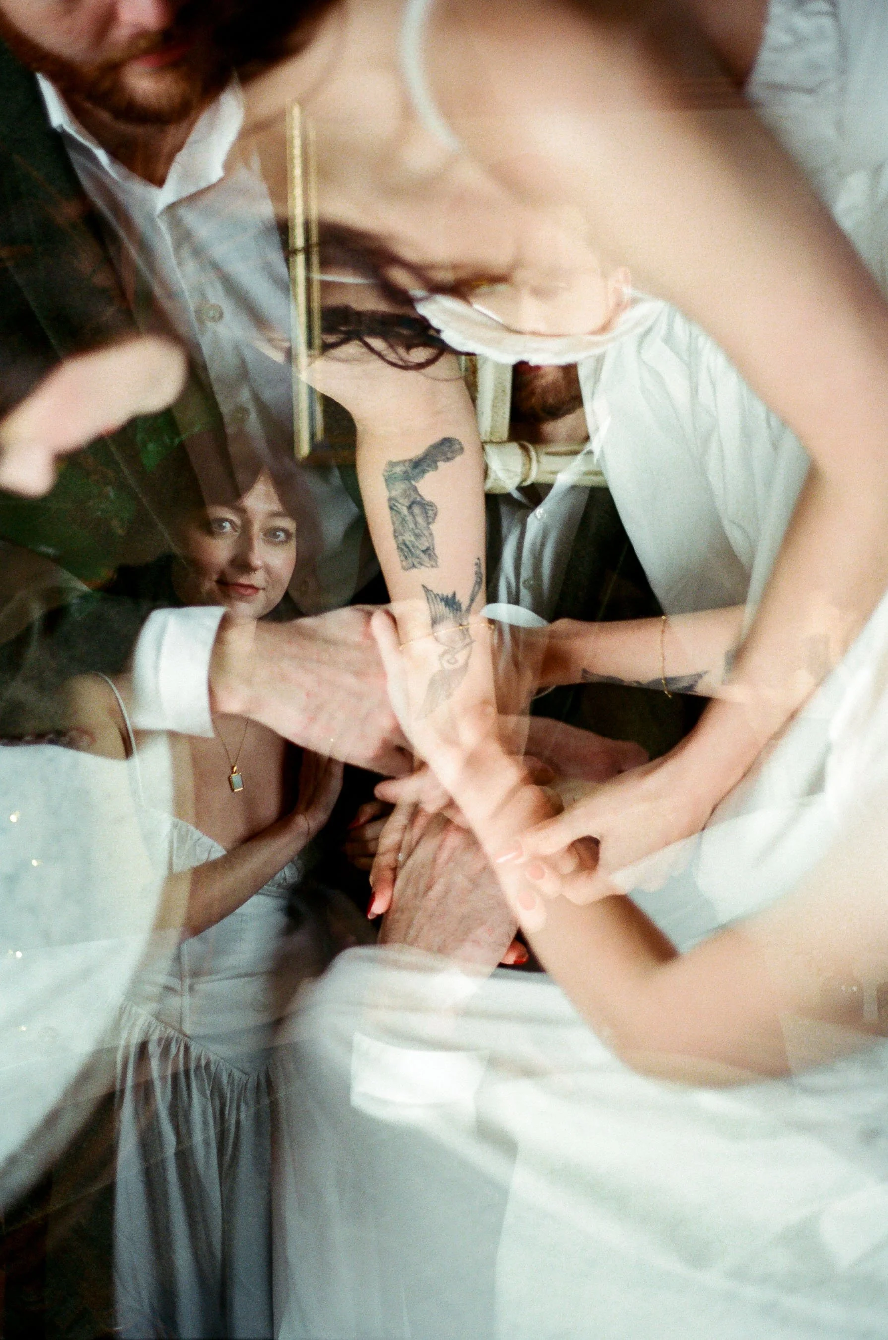 A group of people engaged in a hand gesture, with overlapping reflections of a woman smiling and sitting in the background.