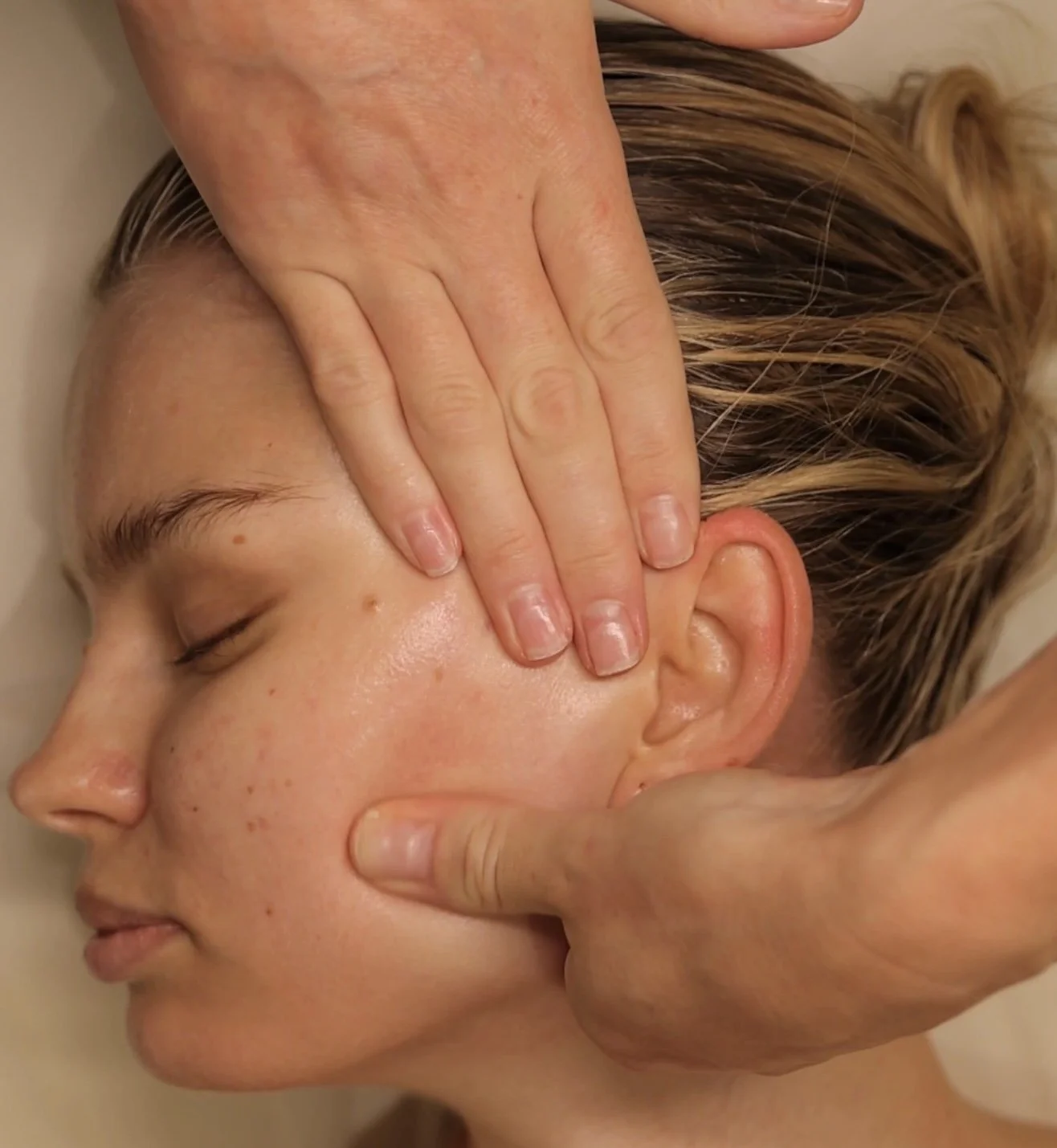 Hands gently massaging a client’s cheek and jaw